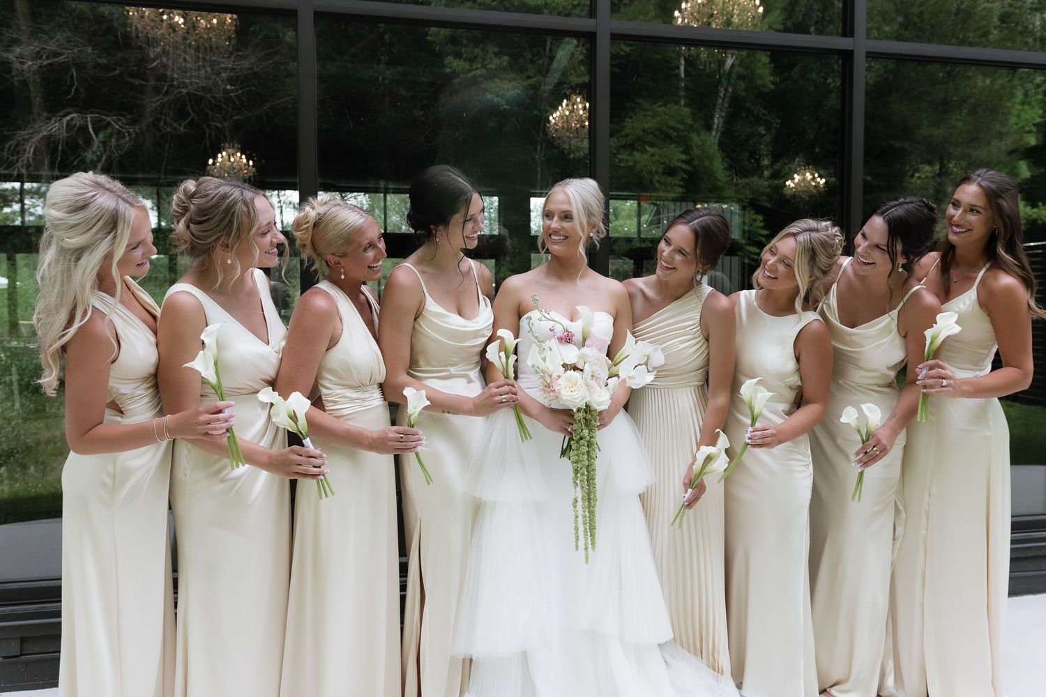 Bride in white gown with bridesmaids in ivory dresses holding bouquets, smiling together outdoors at wedding.