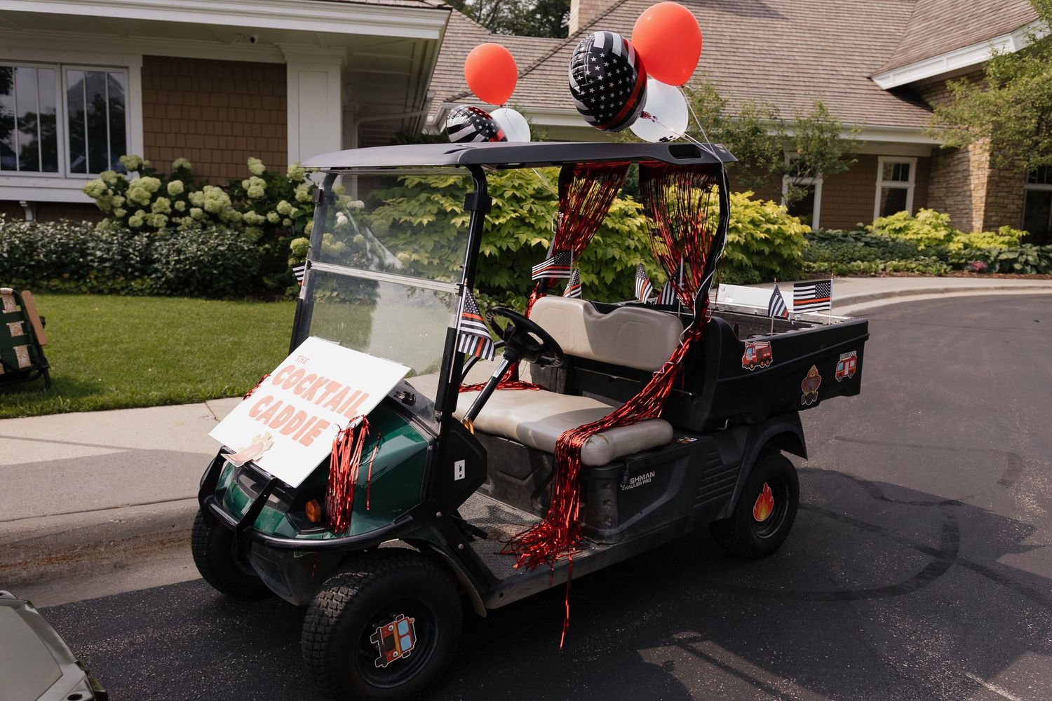 Decorated golf cart with red streamers, disco ball, and orange balloons parked in a suburban driveway.