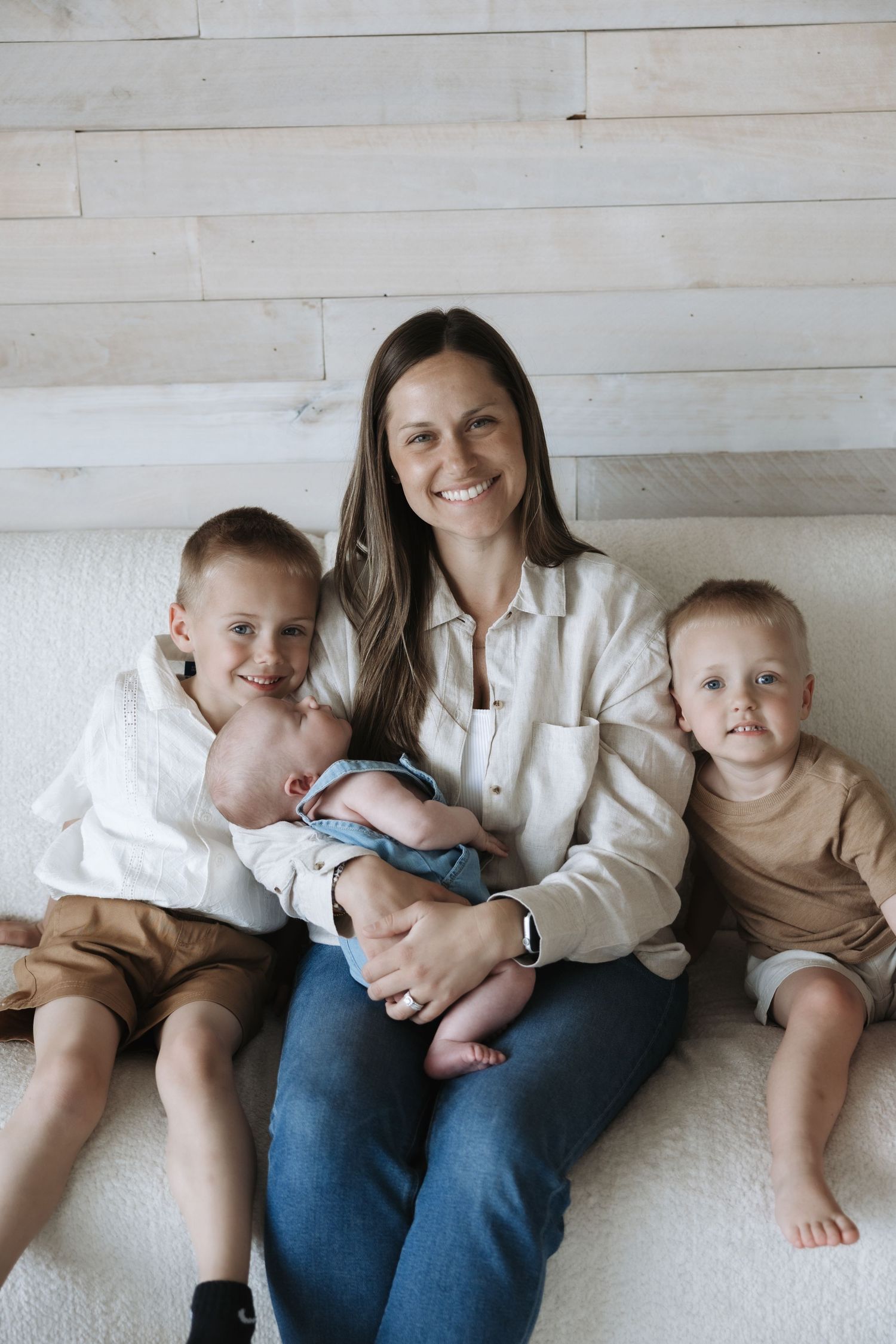 Smiling mother sitting with her three children including a newborn baby on her lap.