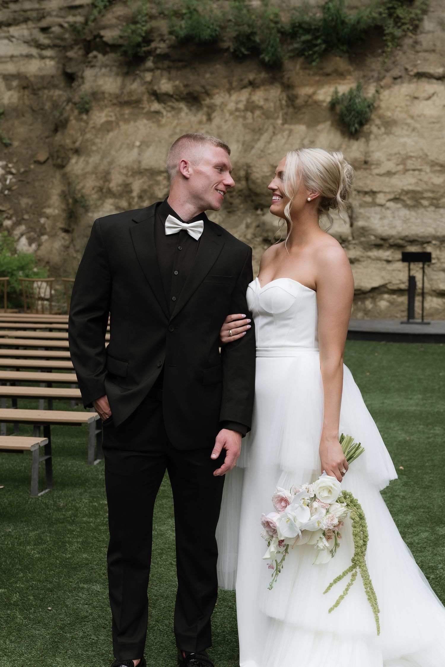 Bride and groom sharing a romantic moment outdoors, she in strapless white gown holding floral bouquet.