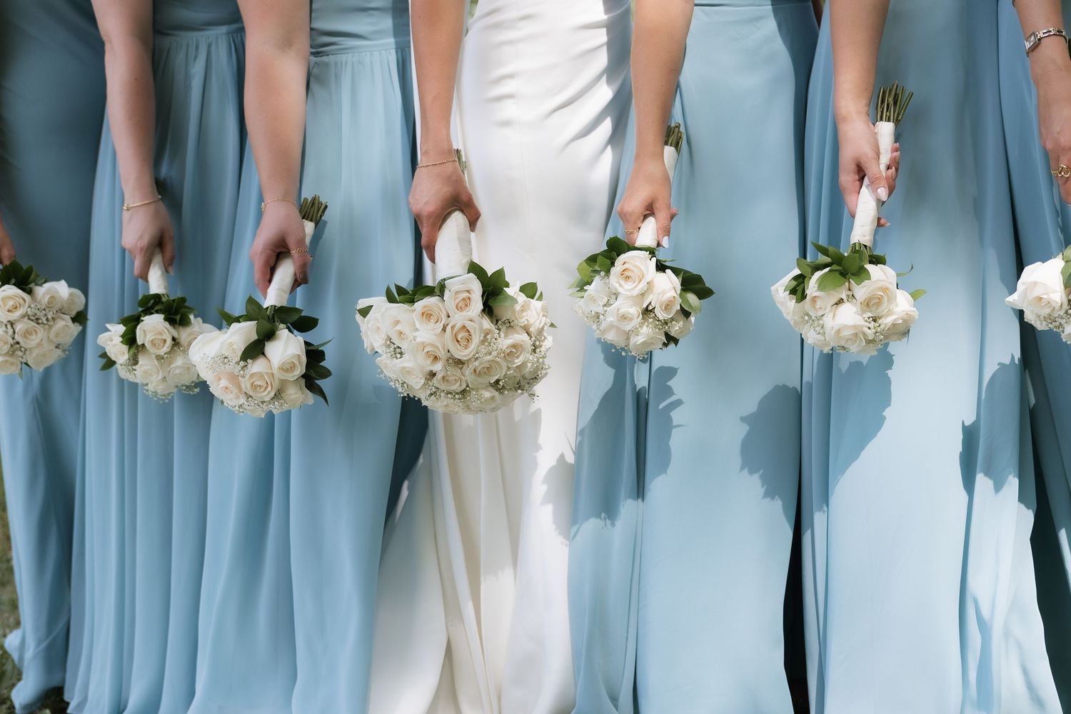 Close-up of bride and bridesmaids in blue gowns holding matching white rose bouquets.