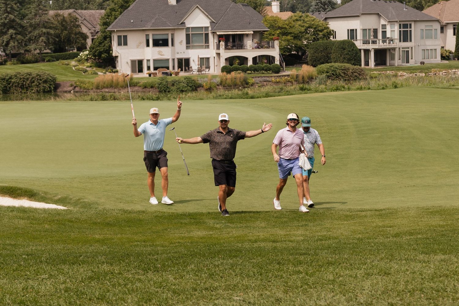 Four golfers celebrating on a lush green golf course with a large luxury home in the background.