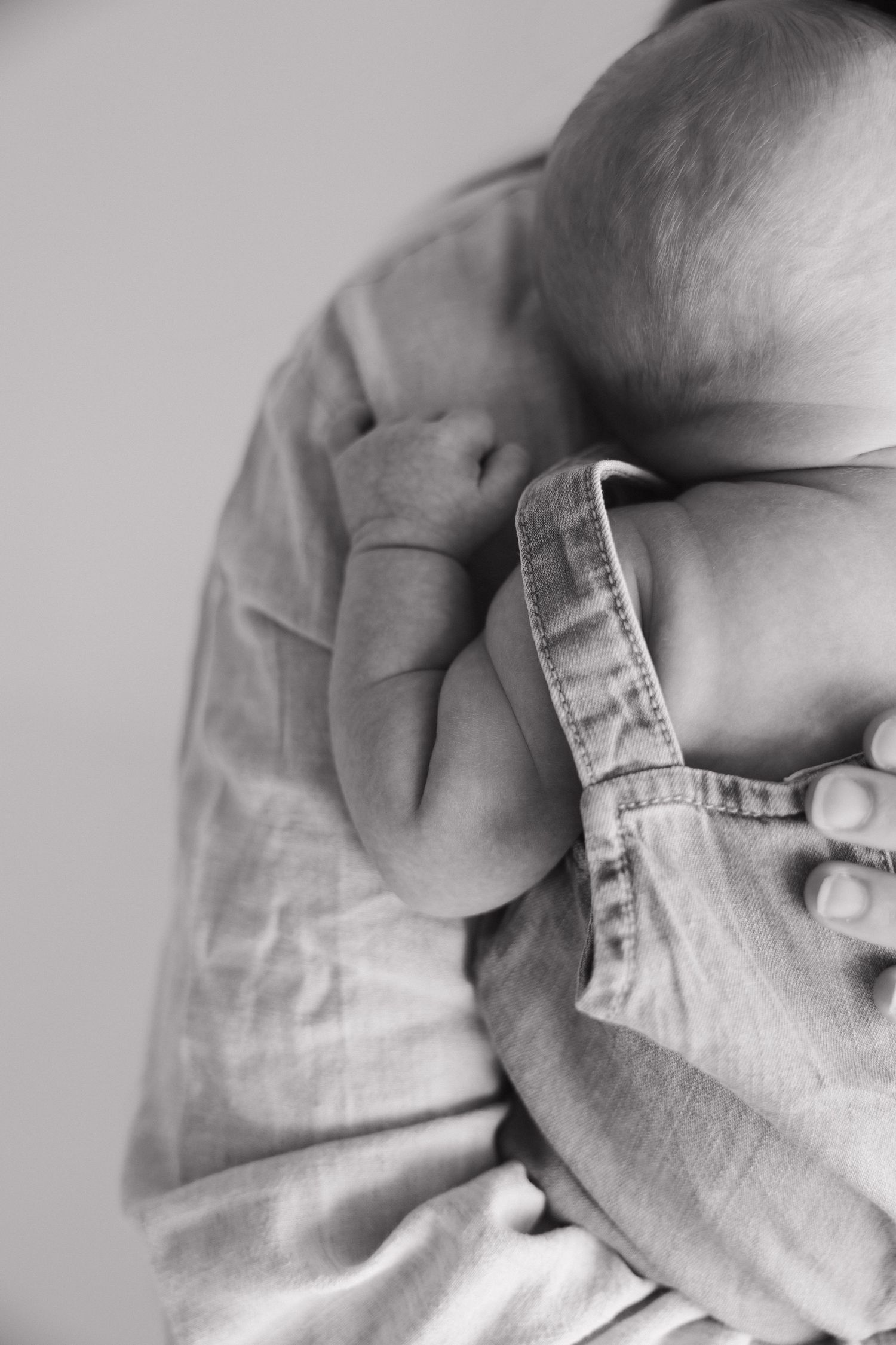 Black and white close-up of a newborn baby being cradled in a parent's arms.