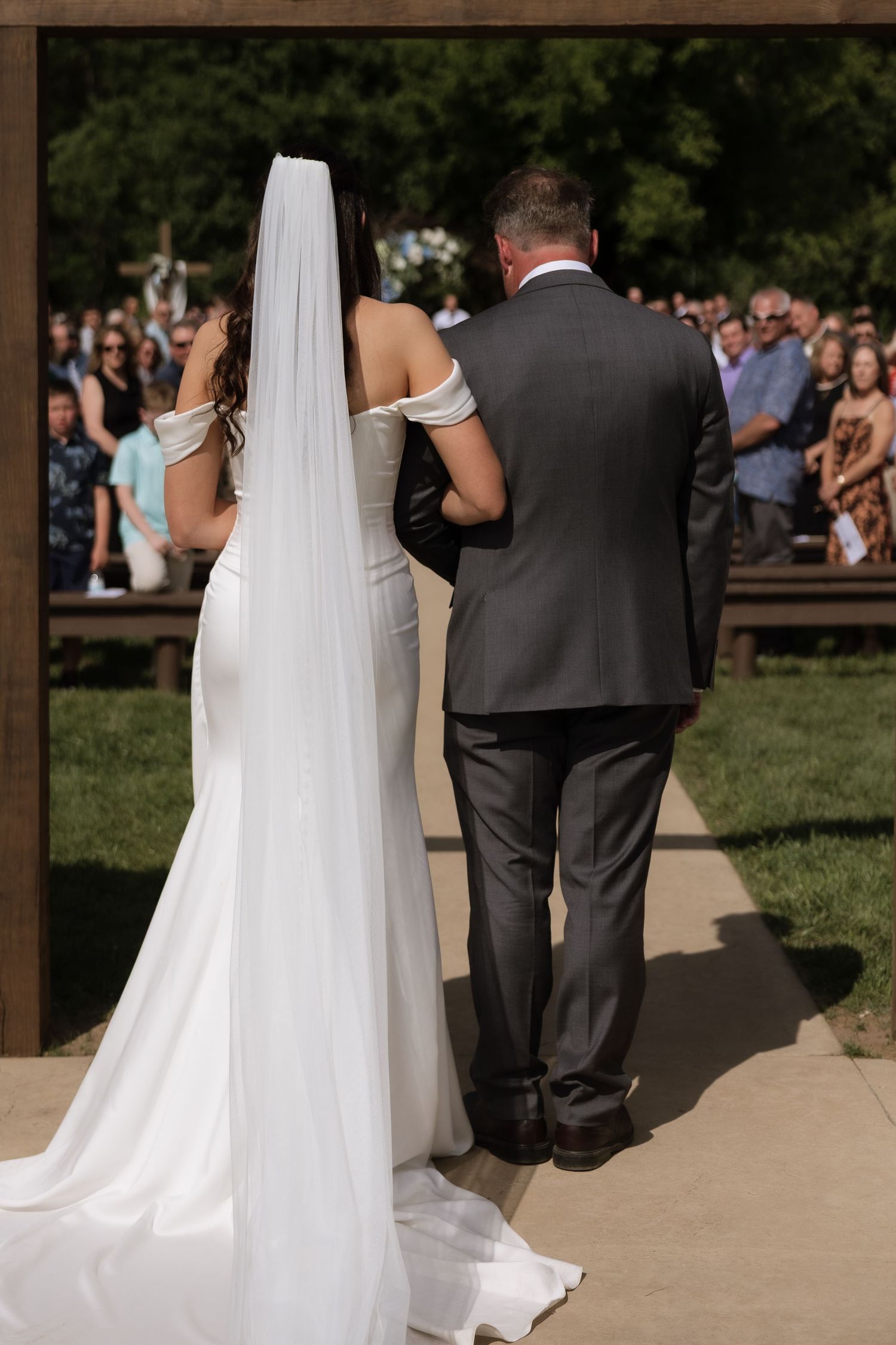 Bride in a white gown with long veil walks arm in arm down the aisle with a man in a gray suit.