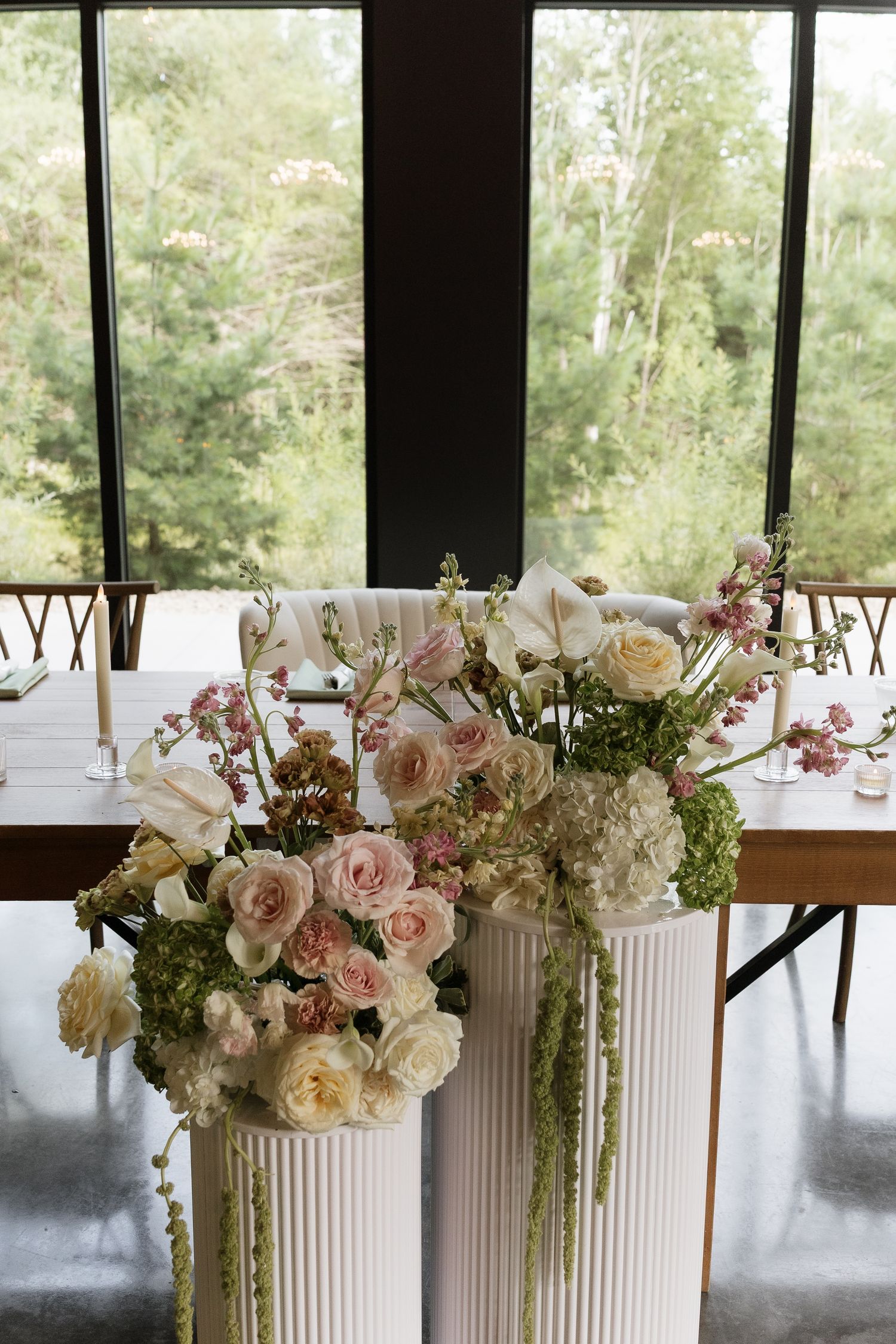 Lush floral centerpiece with pink and white roses on white pedestals at an elegant wedding reception table.