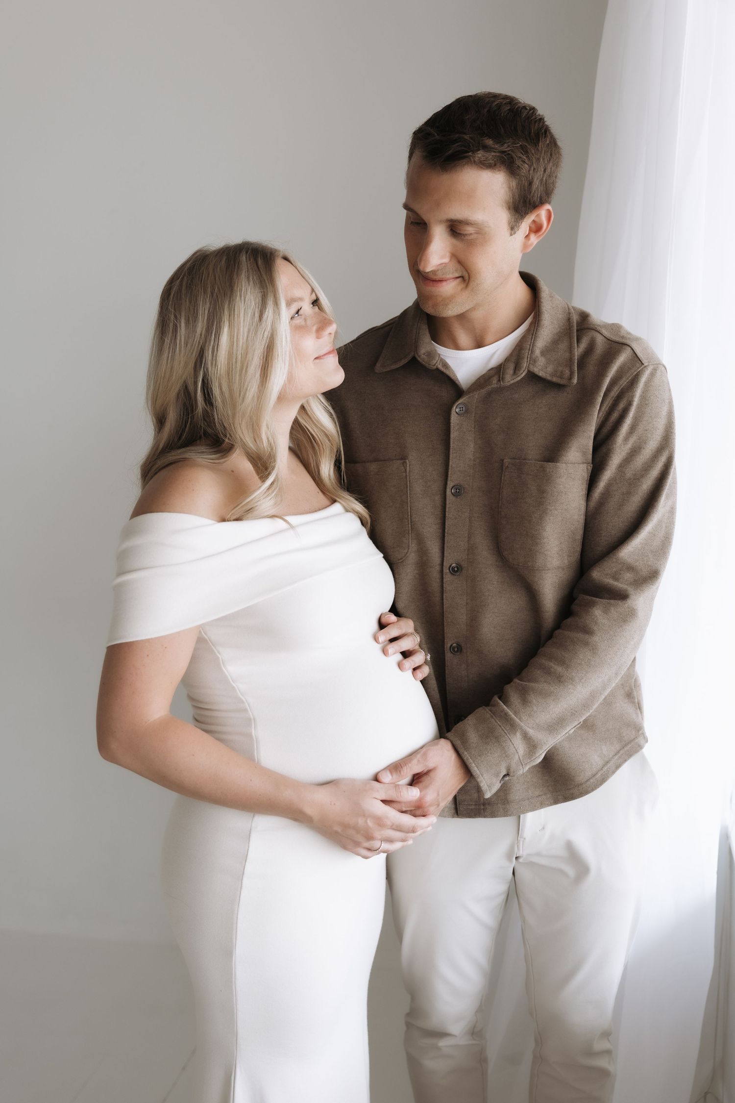 Pregnant couple in neutral tones sharing a gentle gaze during maternity portrait session.