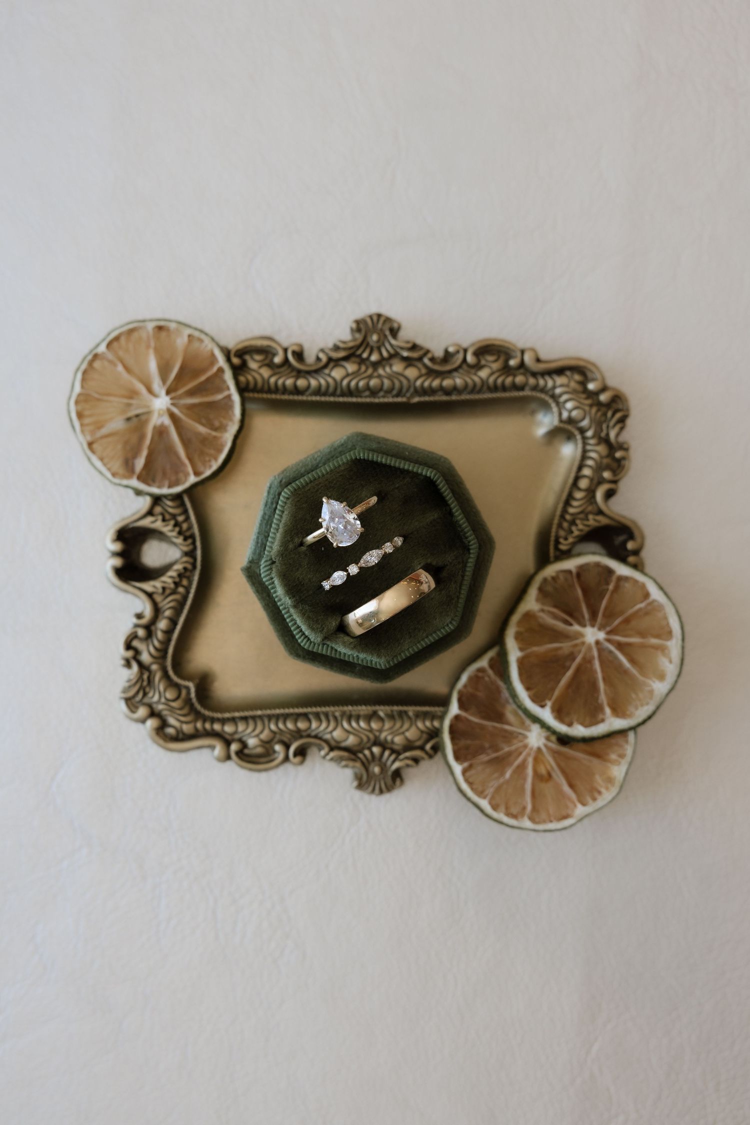Elegant engagement ring set in green velvet box on ornate gold tray with dried citrus slices.