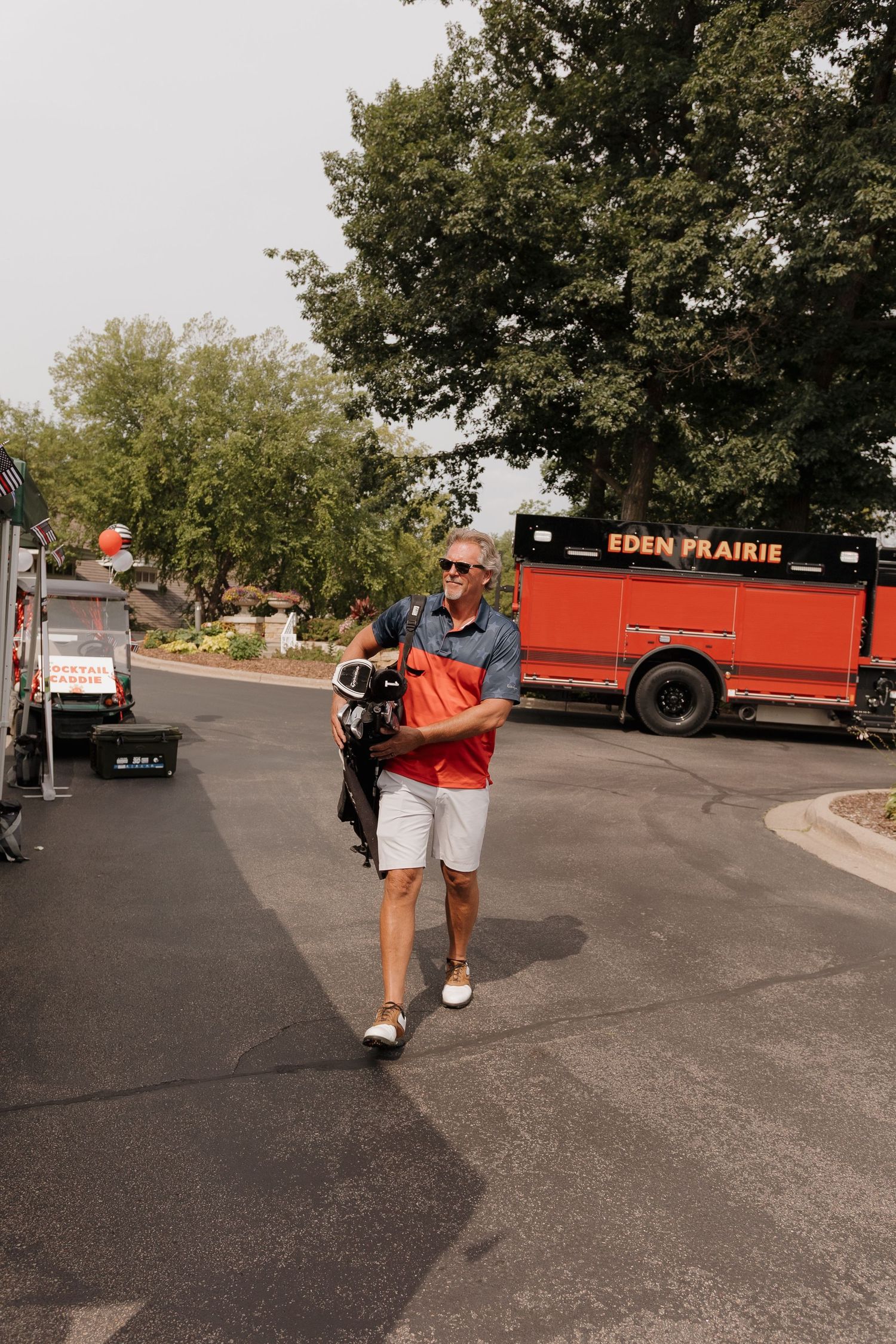 Man in polo shirt carrying golf bag near Eden Prairie truck on sunny day.