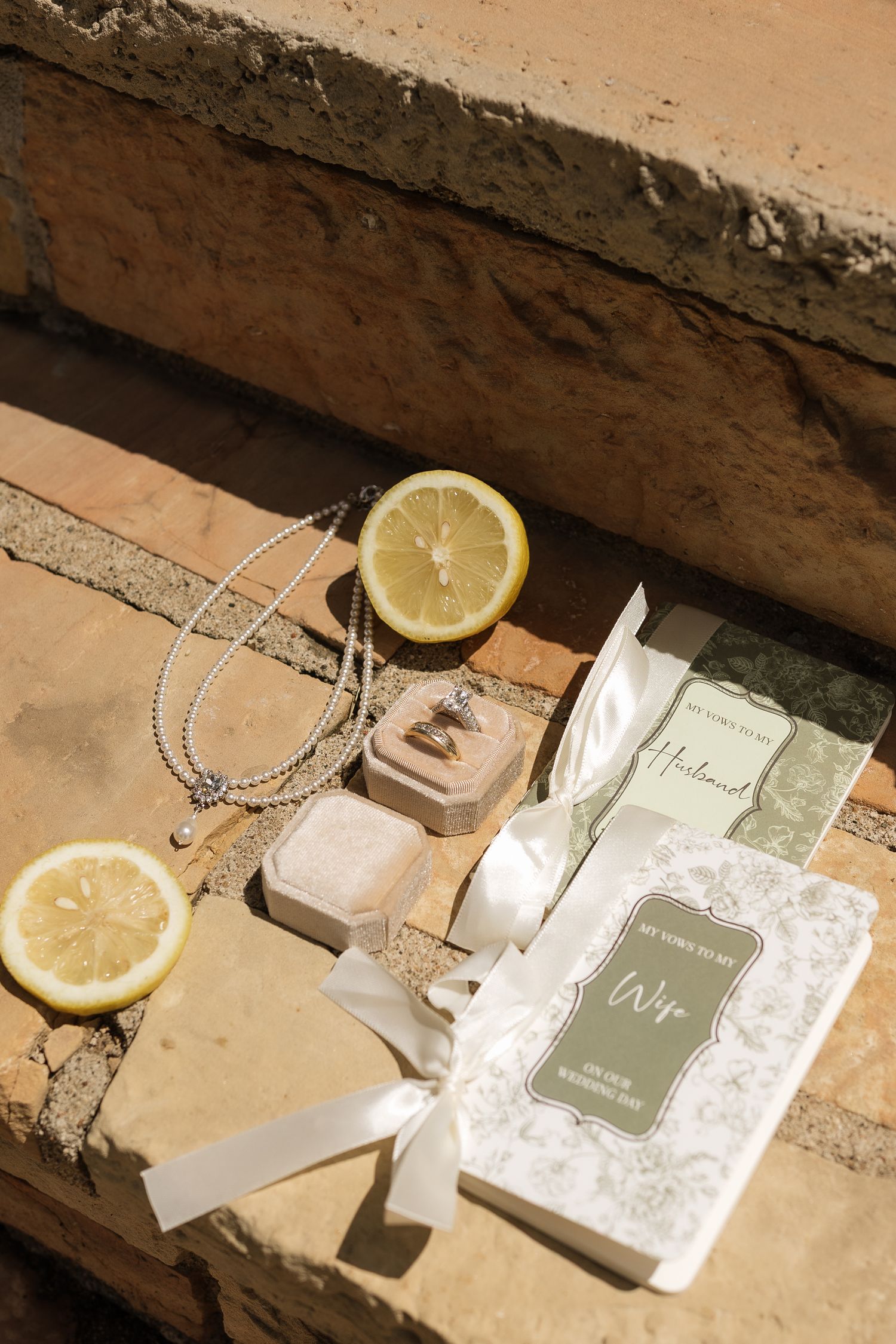 Wedding flat lay with ring box, pearl necklace, lemon slices, and gift books on stone steps.