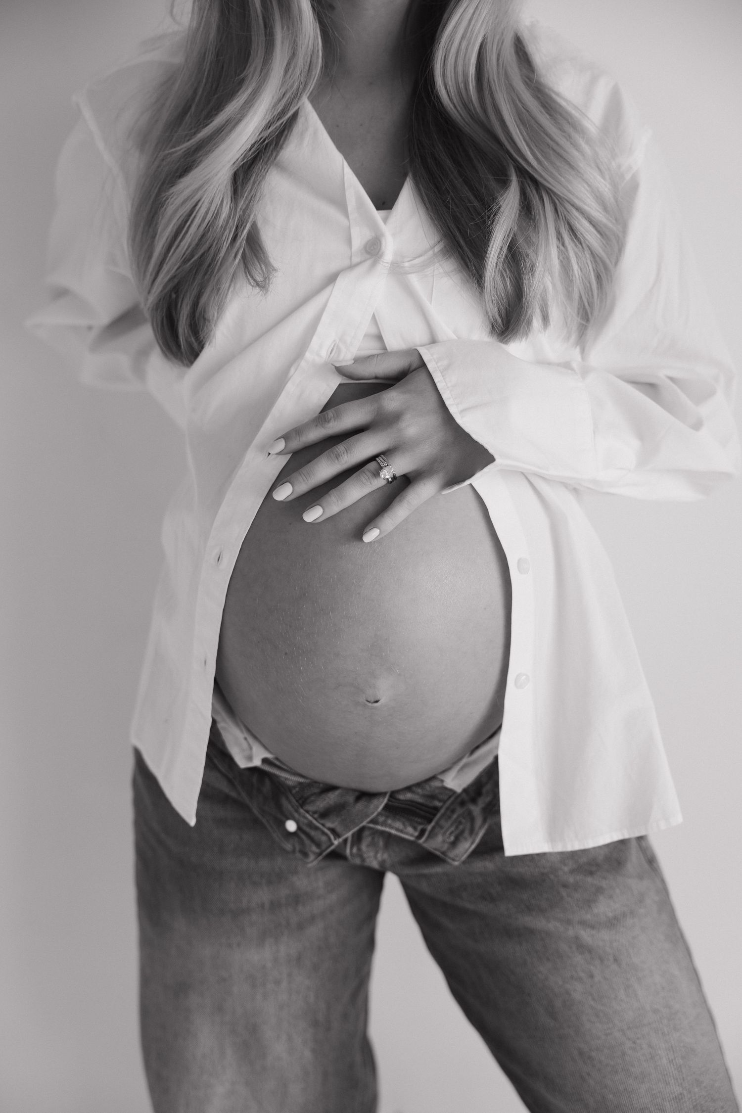 Black and white close-up of pregnant woman in white shirt and jeans gently holding bare baby bump.