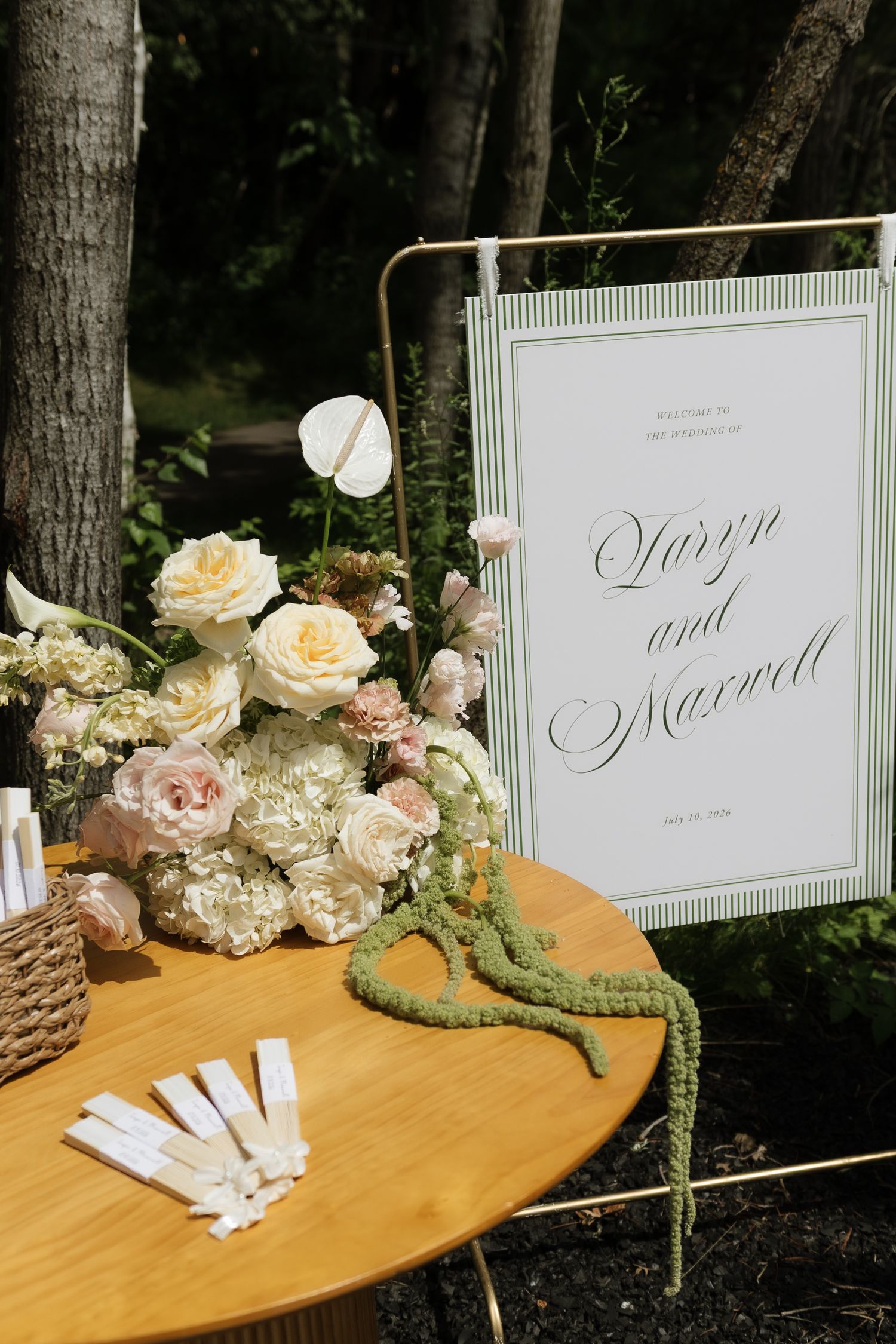 Elegant wedding welcome sign for Quinn and Maxwell displayed with lush pink, white, and cream floral arrangements outdoors.
