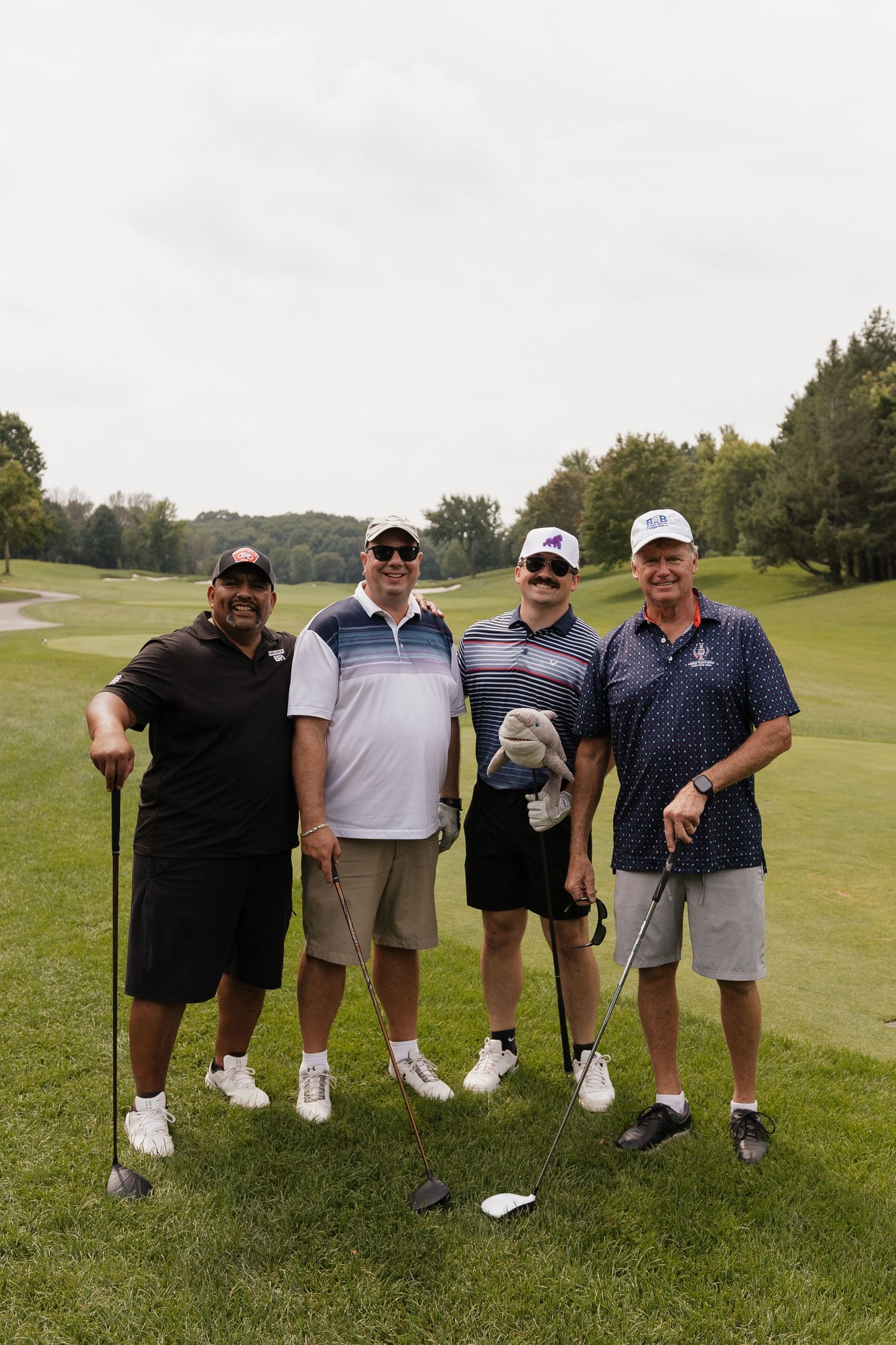Four men posing with golf clubs on a lush green golf course on a cloudy day.