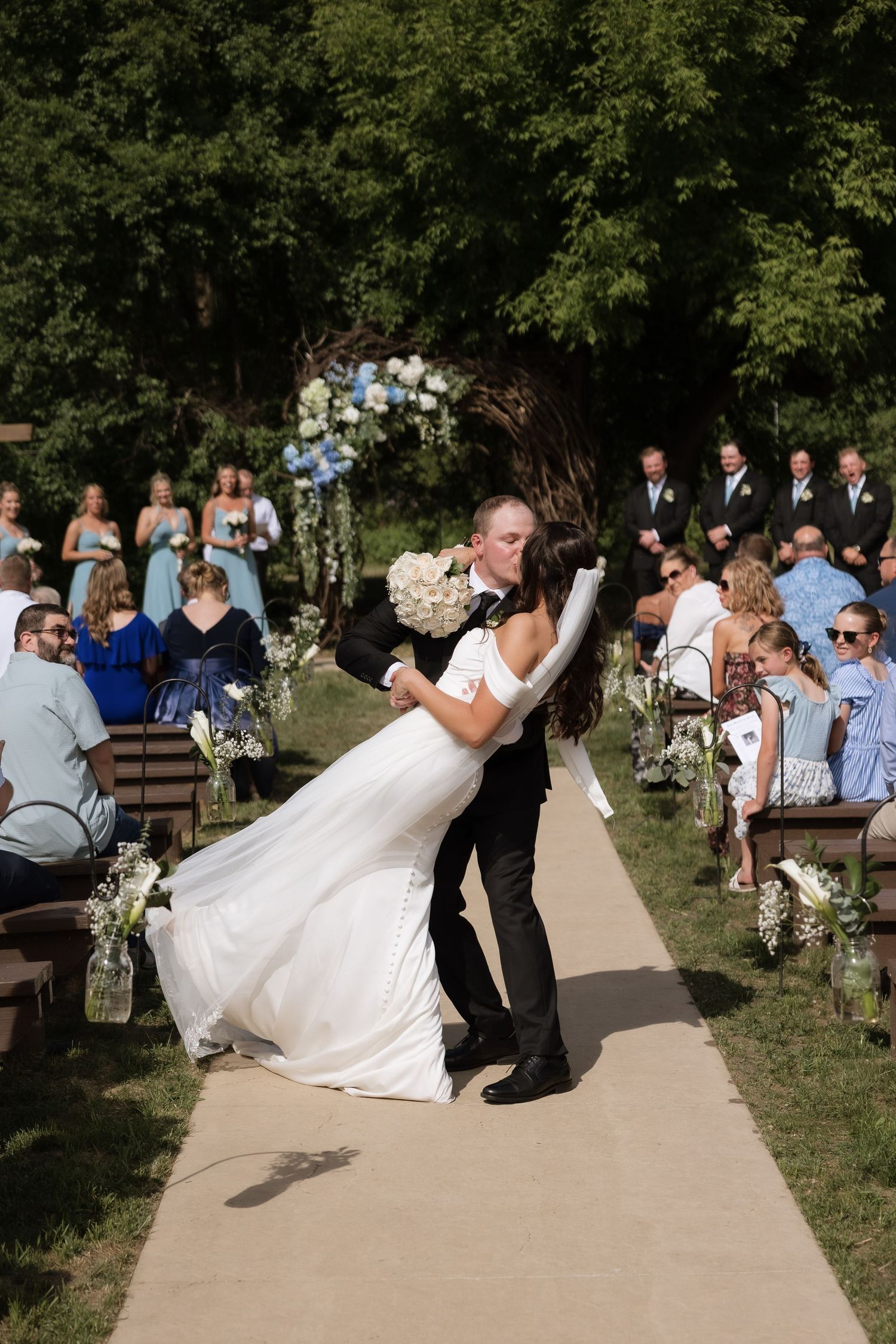 Groom dips bride in white gown during romantic outdoor wedding ceremony kiss at the altar.