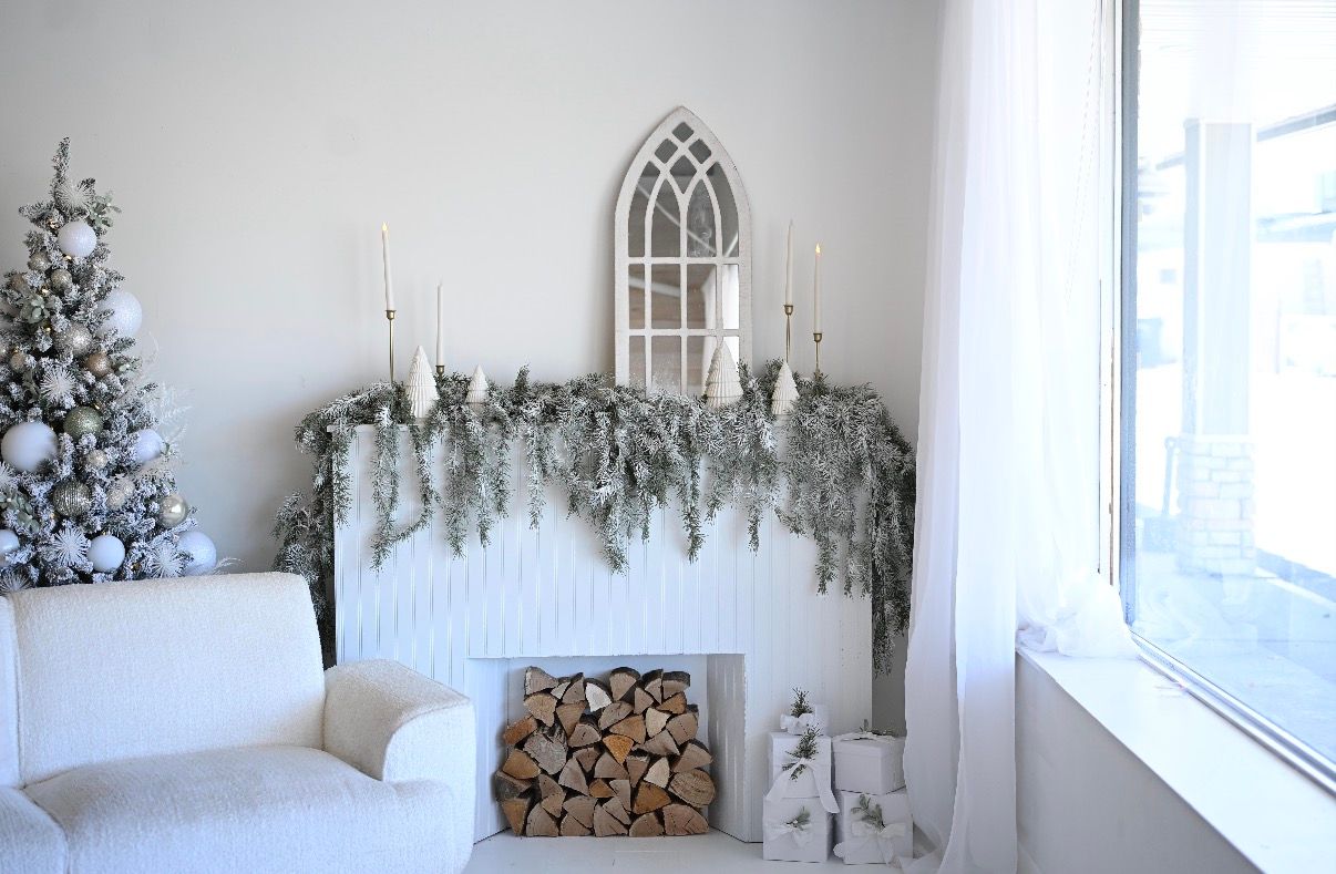 White Christmas mantel with snowy garland, candles, birch logs, and a flocked Christmas tree in an elegant winter decor.