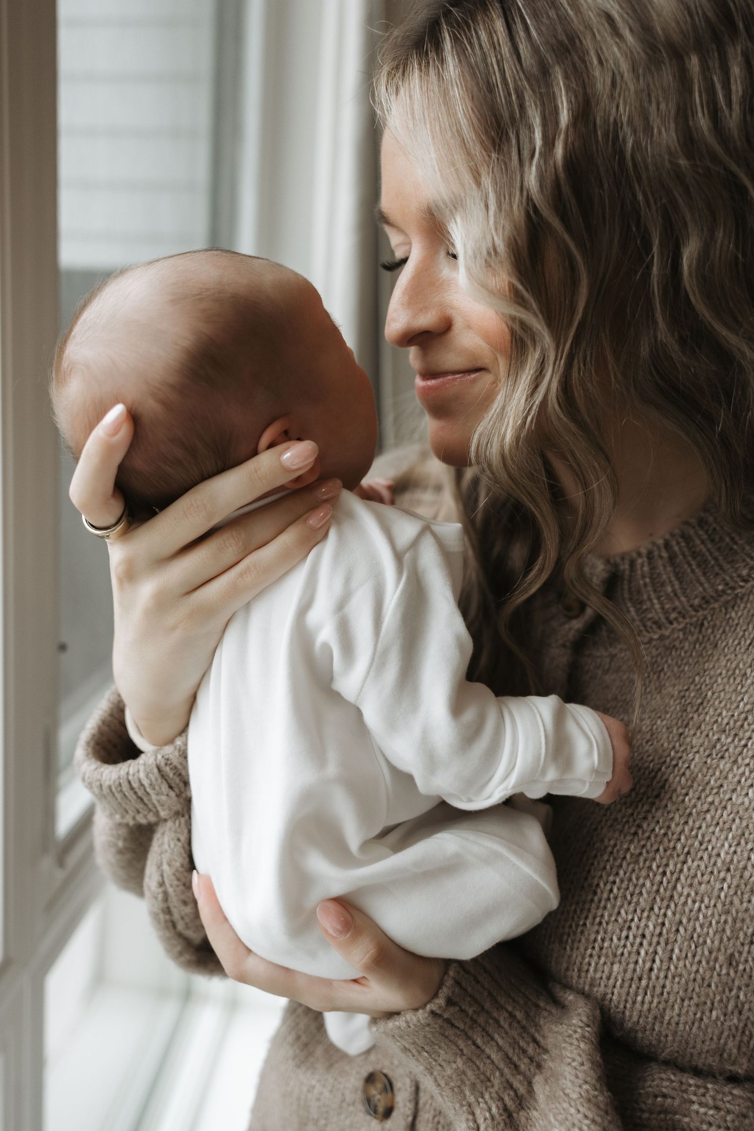 A smiling mother with curly blonde hair tenderly holding her newborn baby.