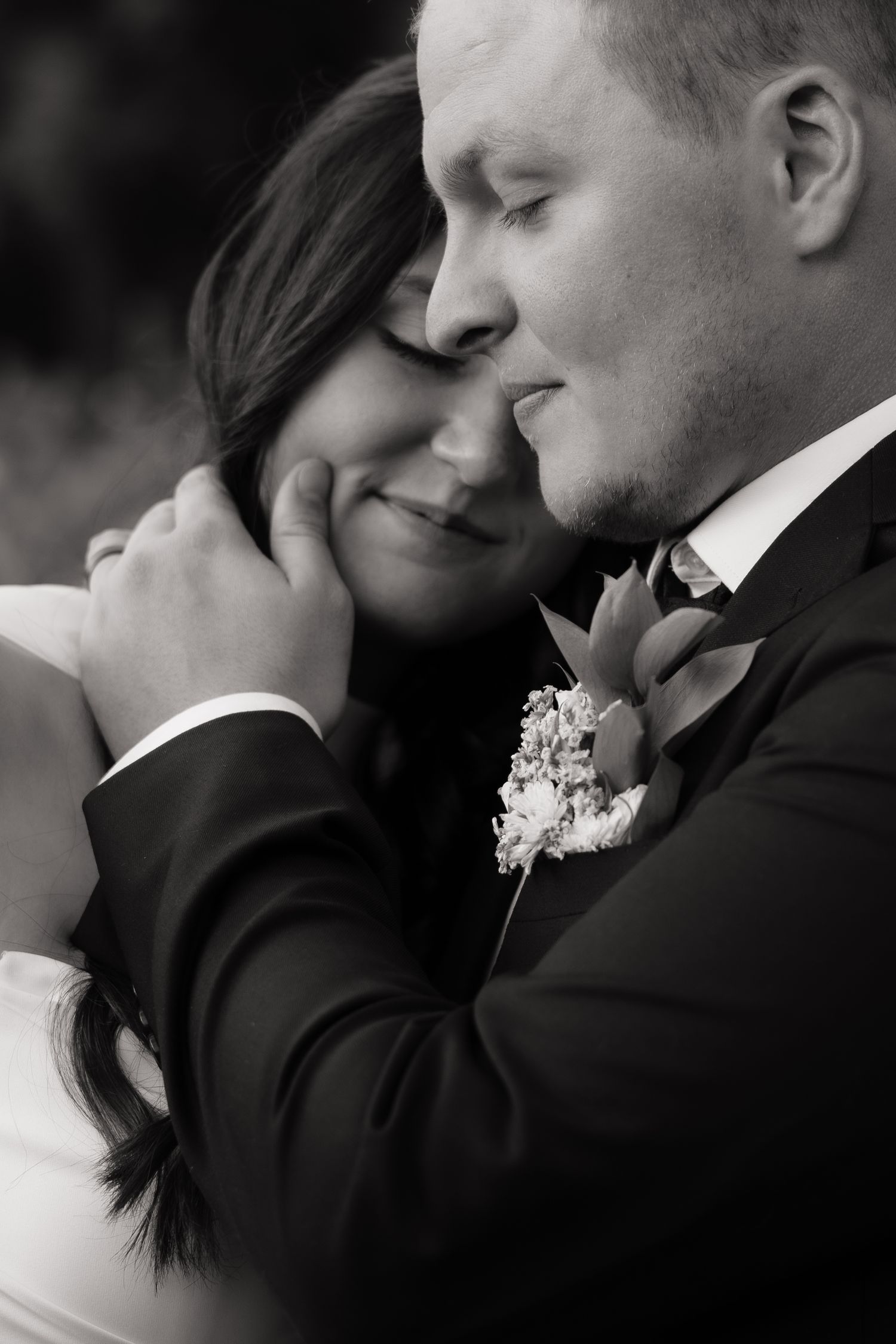 Black and white portrait of bride and groom embracing tenderly with groom cradling bride's face.