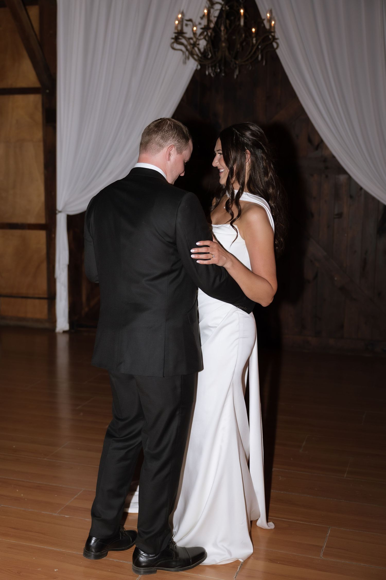 Bride and groom share a joyful first dance moment inside a beautifully draped barn reception venue.
