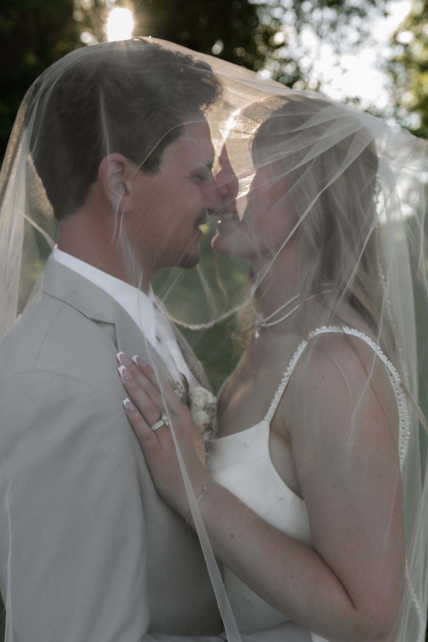 A bride and groom share an intimate moment under a wedding veil outdoors.