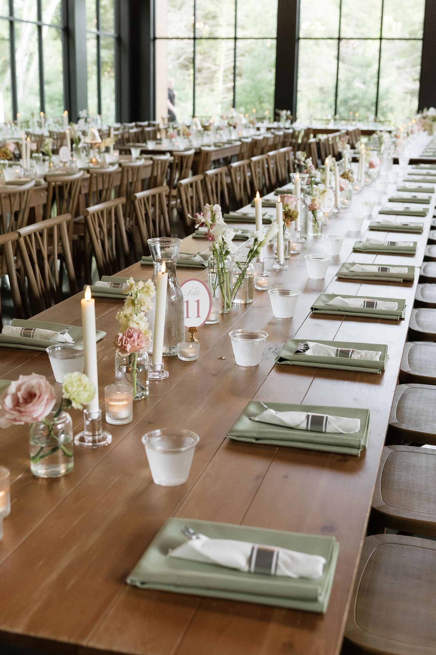 Elegant wedding reception long tables with sage green napkins, candles, and floral centerpieces in a modern venue.