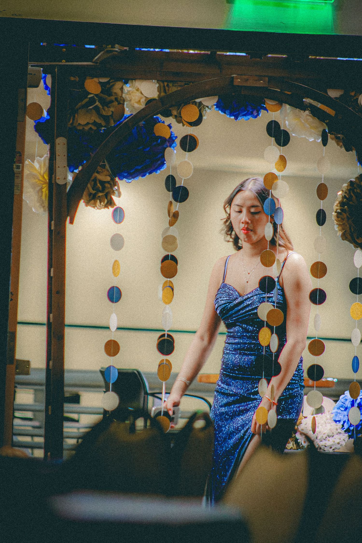 A woman in a blue sequin dress stands beneath circular garland decorations at a formal event.