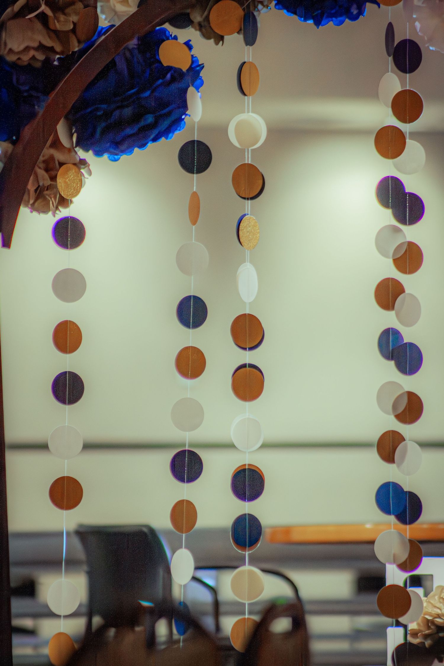 Decorative paper circle garlands in gold, navy, and white hang from a wooden arch indoors.
