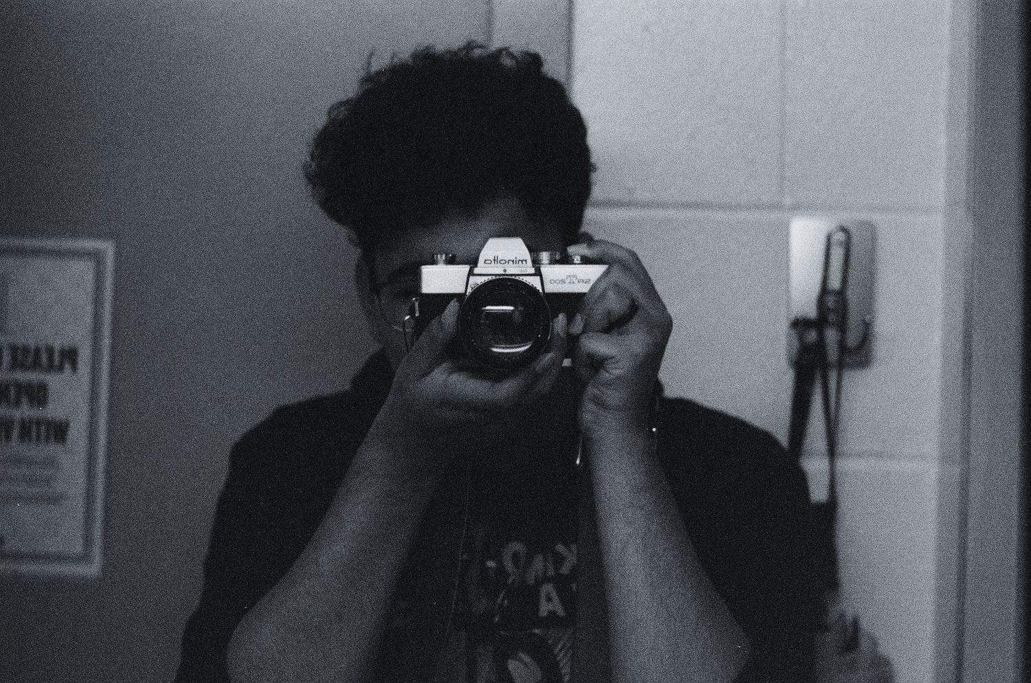 Person taking mirror selfie with vintage film camera in black and white photo.