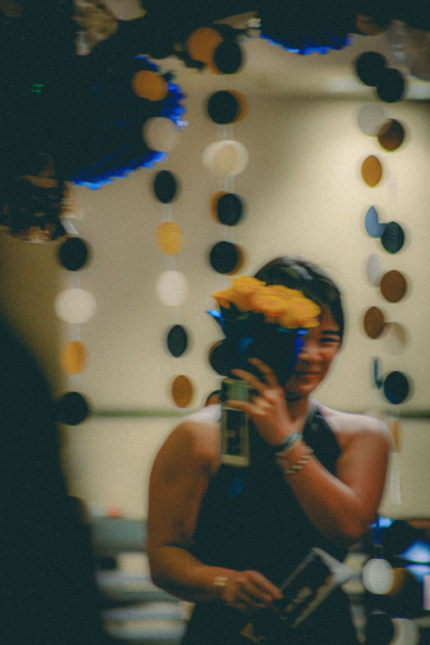 A smiling woman holds yellow flowers and a phone at a decorated indoor event venue.