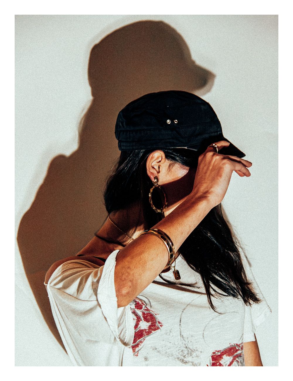 Woman in black cap and floral tee shields face with arm in artistic pose.