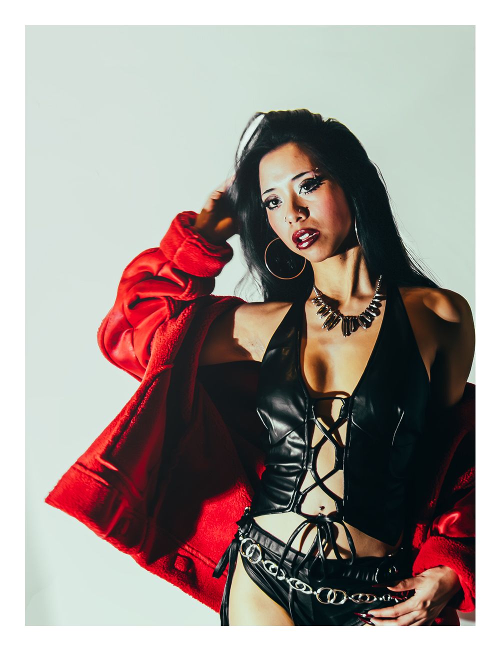 Woman in black leather halter and red jacket poses confidently with hoop earrings.