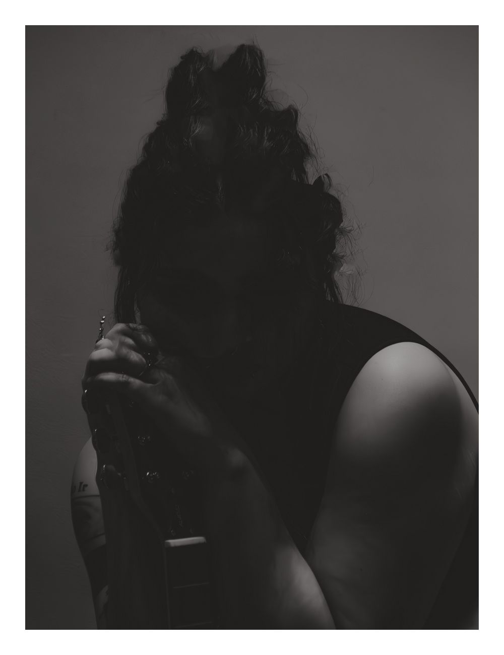 A dramatic black and white portrait of a curly-haired person holding a microphone in shadow.
