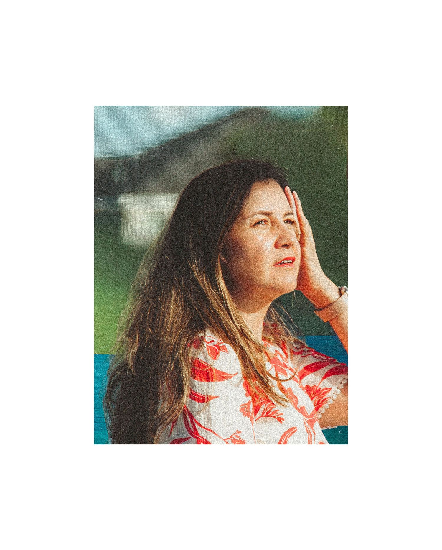 Woman with long brown hair in a floral top gazing upward outdoors in warm golden light.