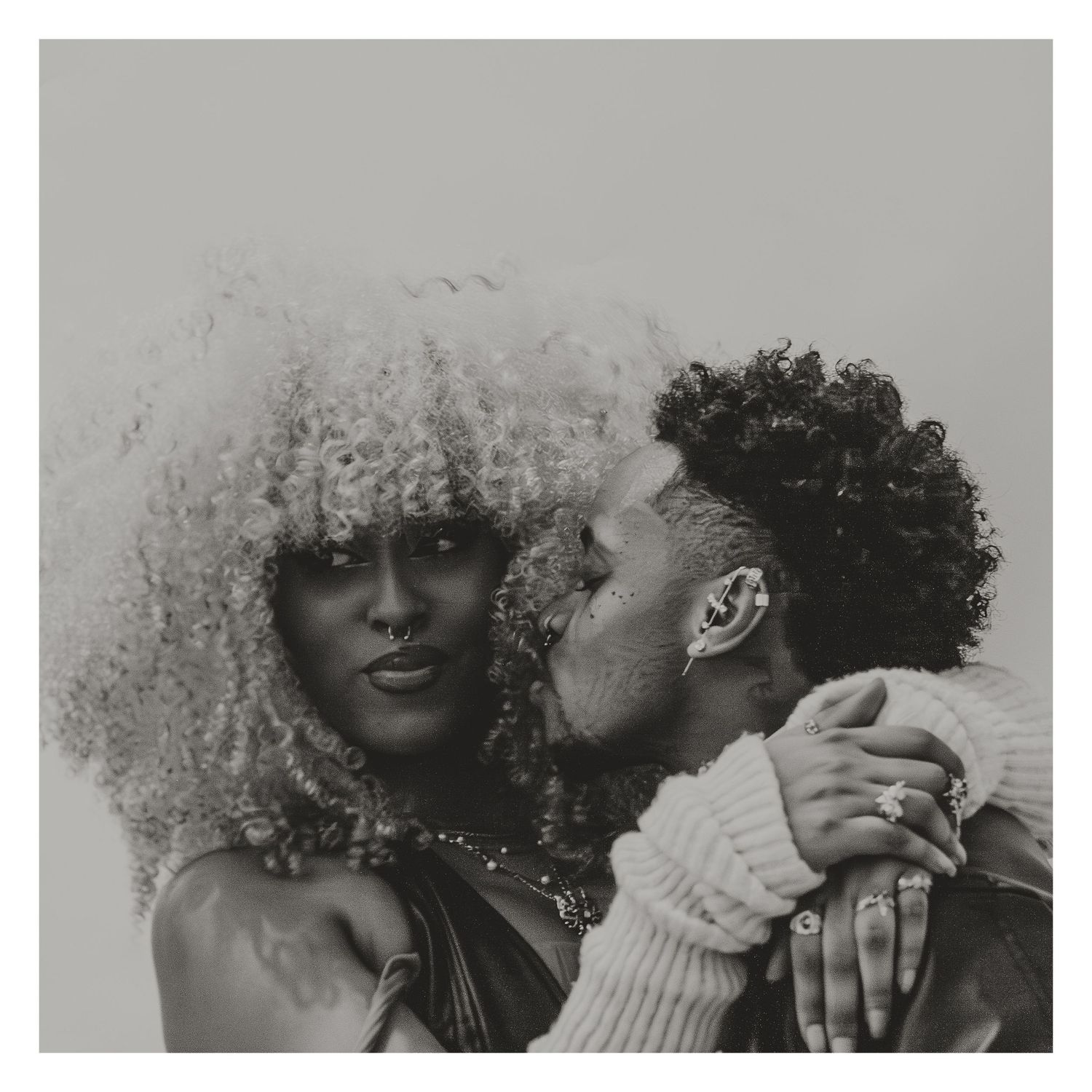 Black and white photo of a woman with afro hair being kissed on the cheek.
