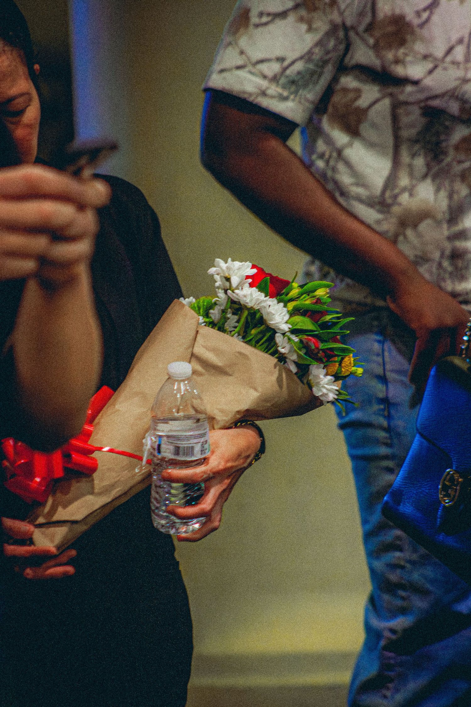 A person holds a bouquet of white and red flowers wrapped in brown paper at an indoor event.
