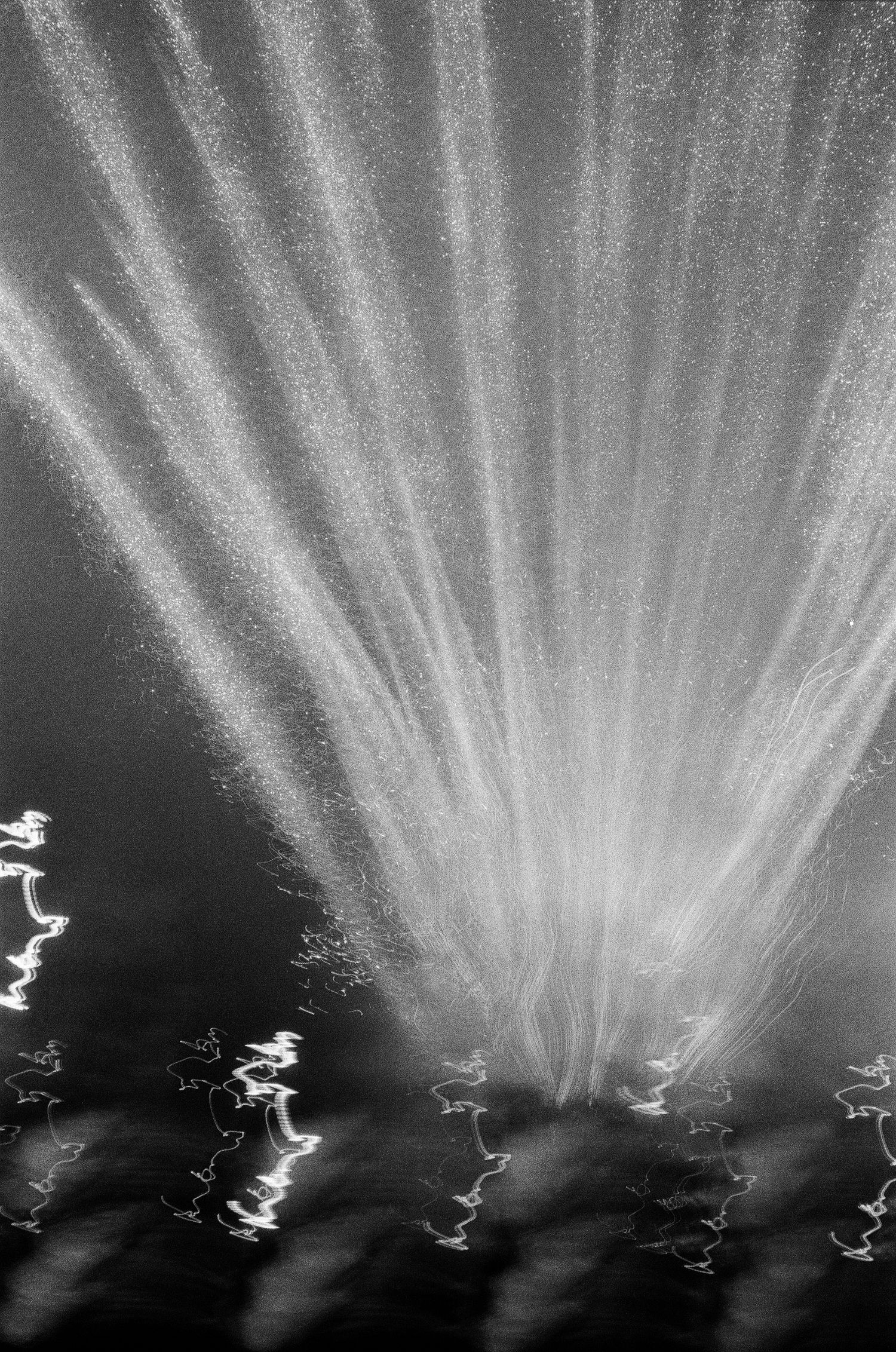 Black and white long exposure photograph of a water fountain creating dramatic light streaks at night.