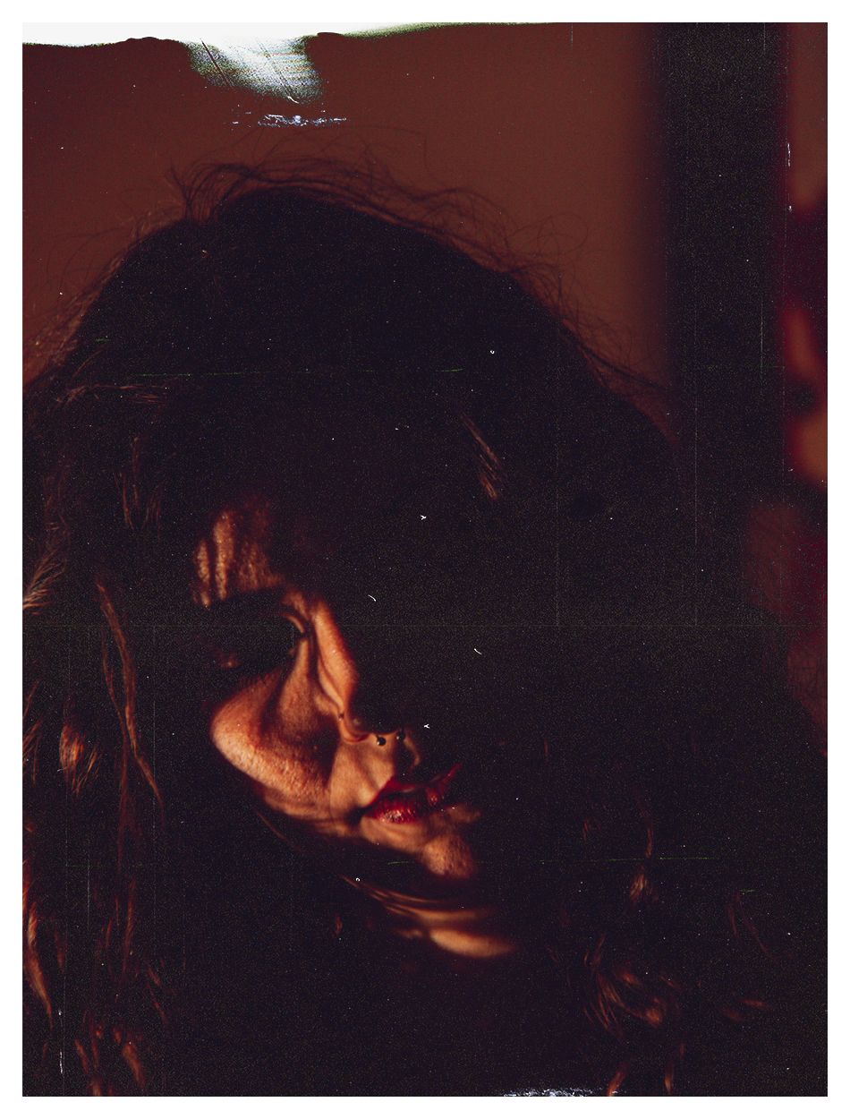 Dramatic dark portrait of a person with tousled hair and red lips partially illuminated by warm light.