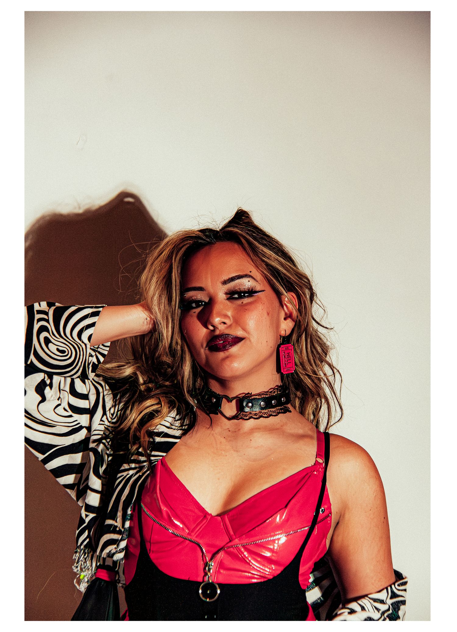 Blonde woman in pink latex top, zebra print jacket, and black choker poses boldly.