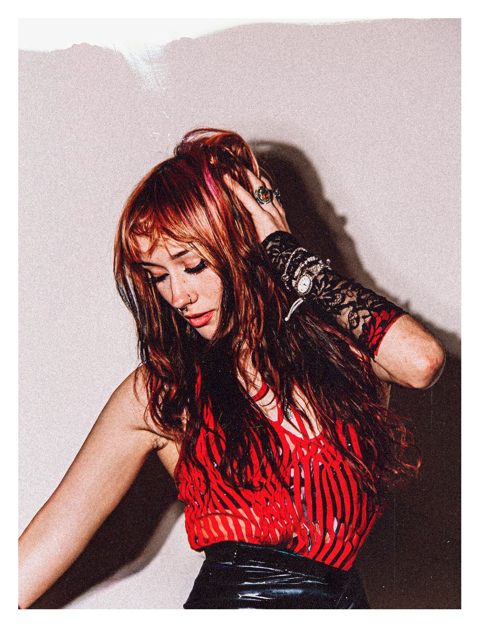 A woman with vibrant red hair dances in a red striped top and black vinyl skirt.