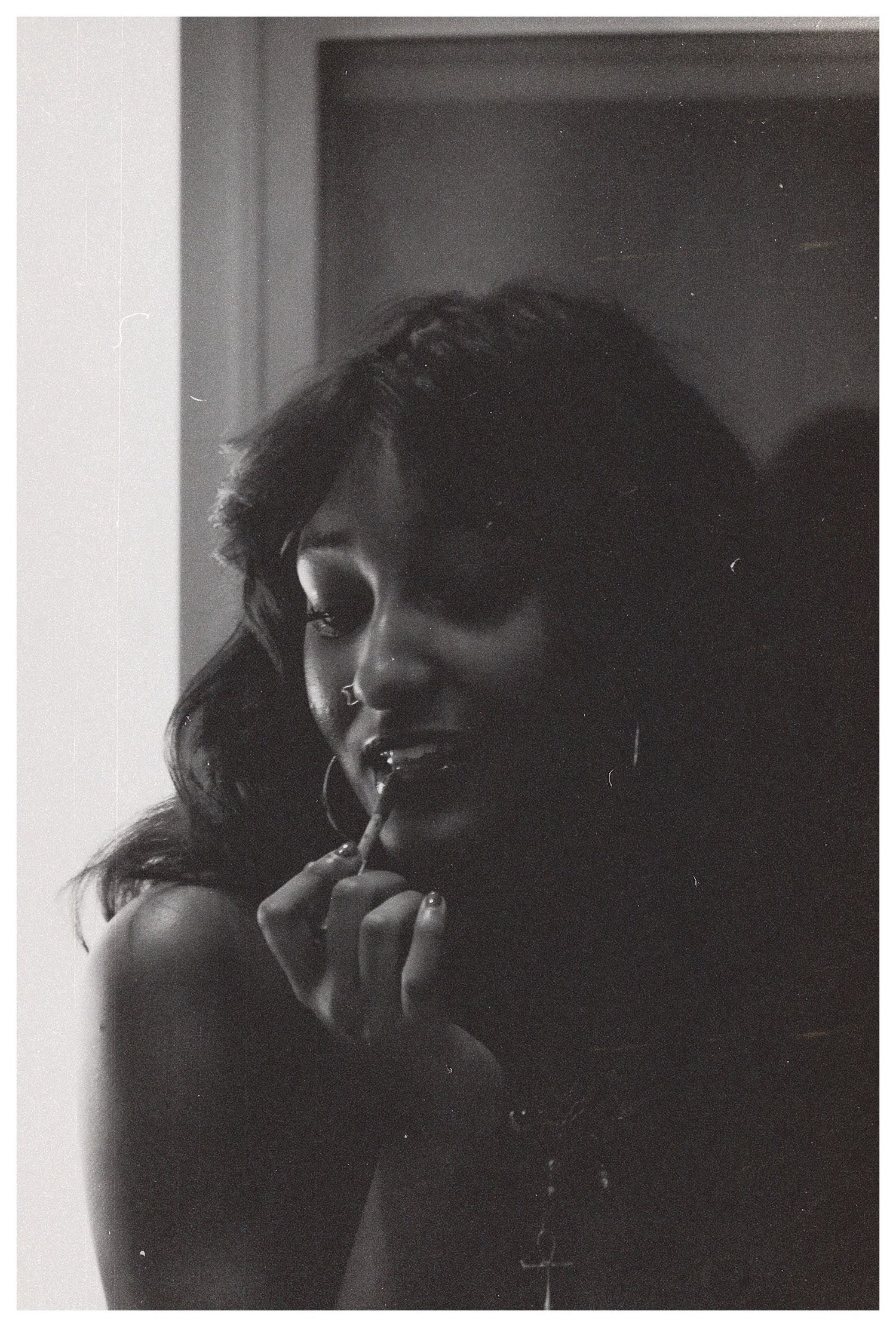 A black and white portrait of a woman smiling softly near a window in dim light.