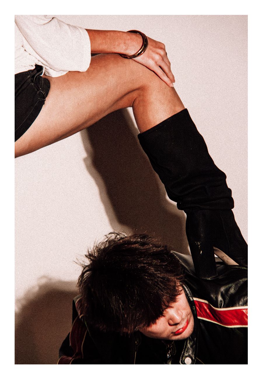 Close-up of woman in black knee-high boots posing over a man in leather jacket in fashion editorial.