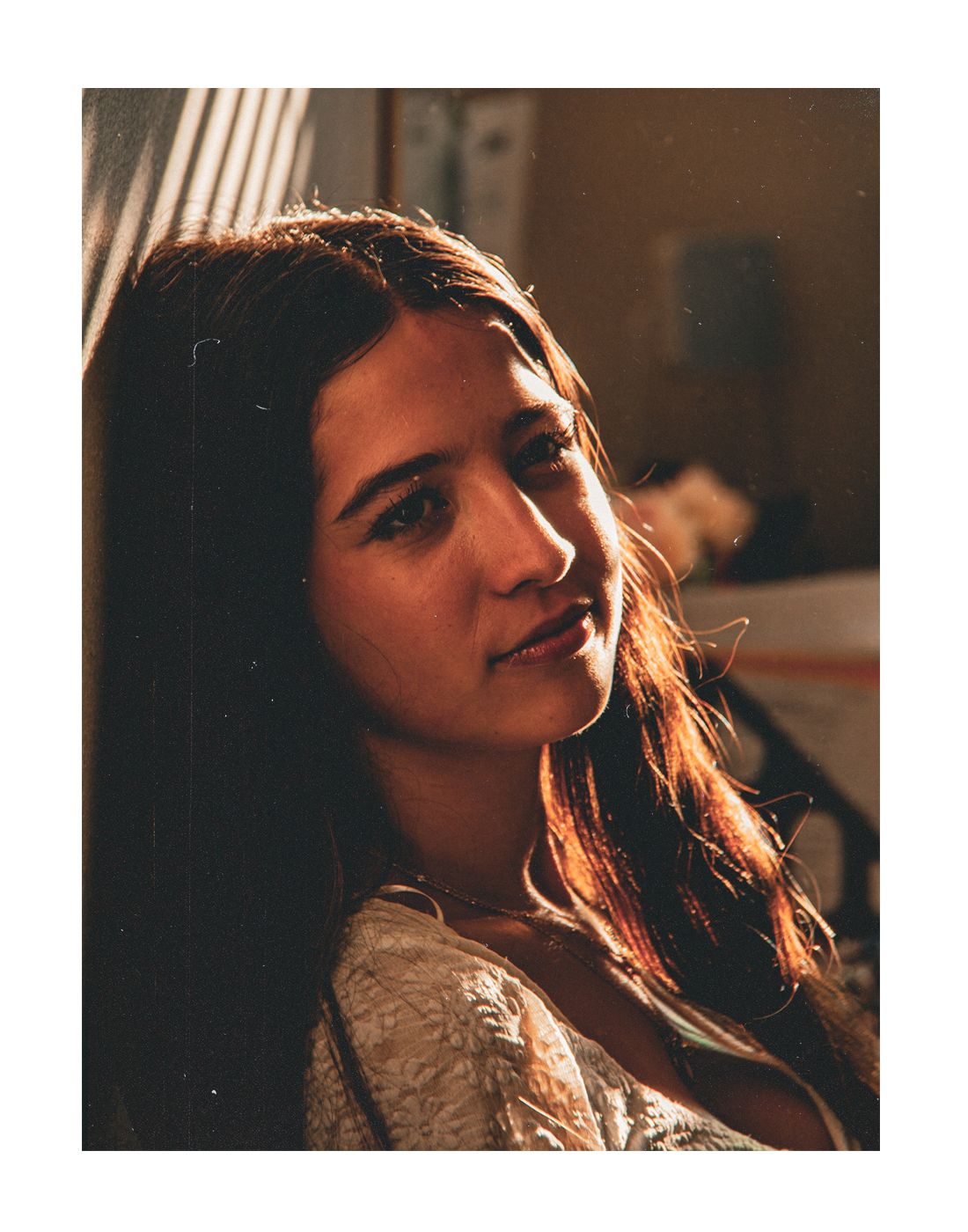 Close-up portrait of a young woman with brown hair illuminated by warm golden side lighting indoors.