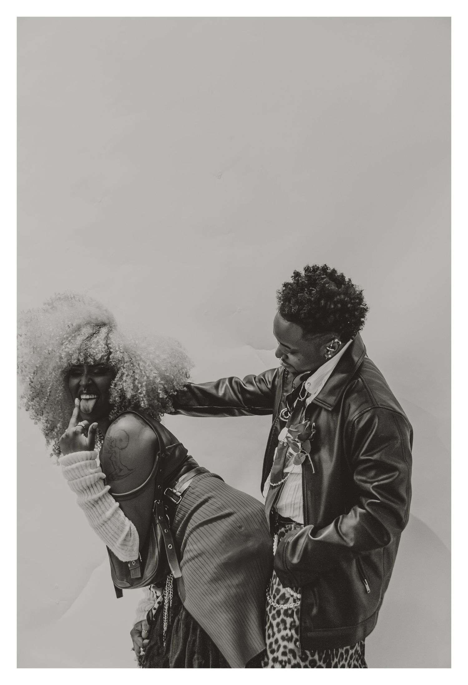 Black and white photo of two models in leather jackets interacting playfully in a fashion editorial.