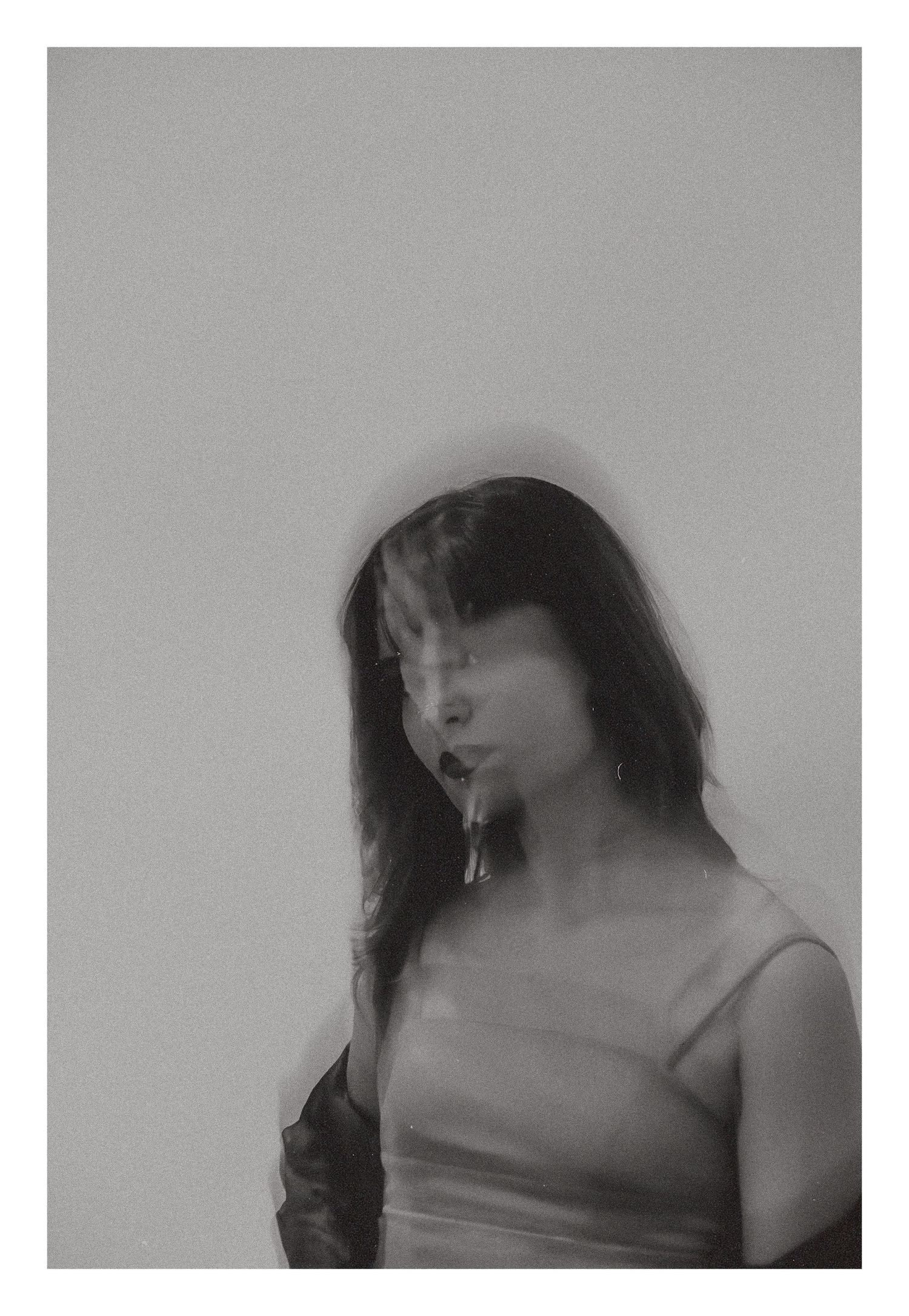Blurred black and white portrait of woman in slip dress against gray background.