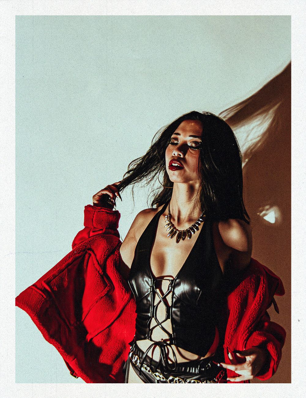 Woman in black corset and red jacket posing dramatically against a light background.