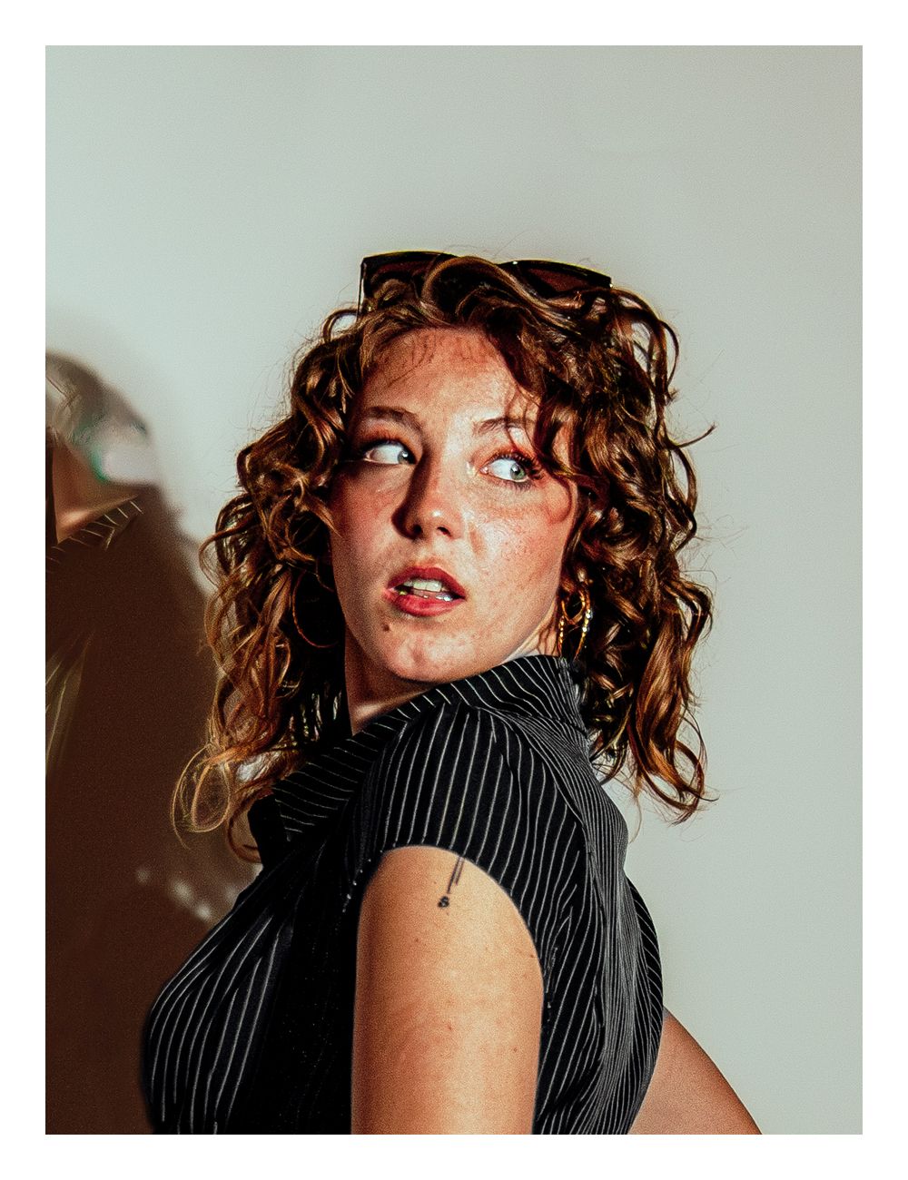Young woman with curly auburn hair in a pinstripe top gazing over her shoulder.