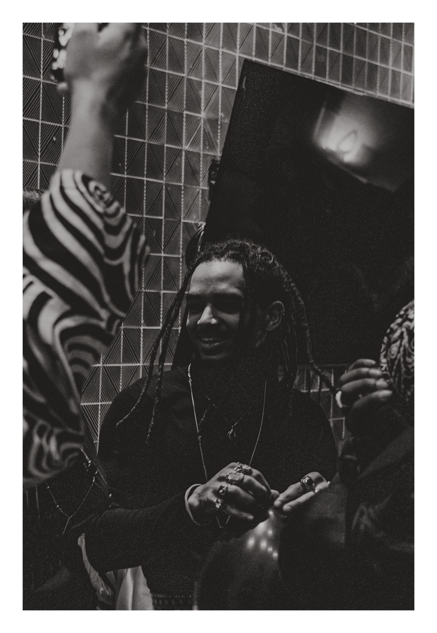 A black and white candid photo of a man with dreadlocks laughing with friends backstage.