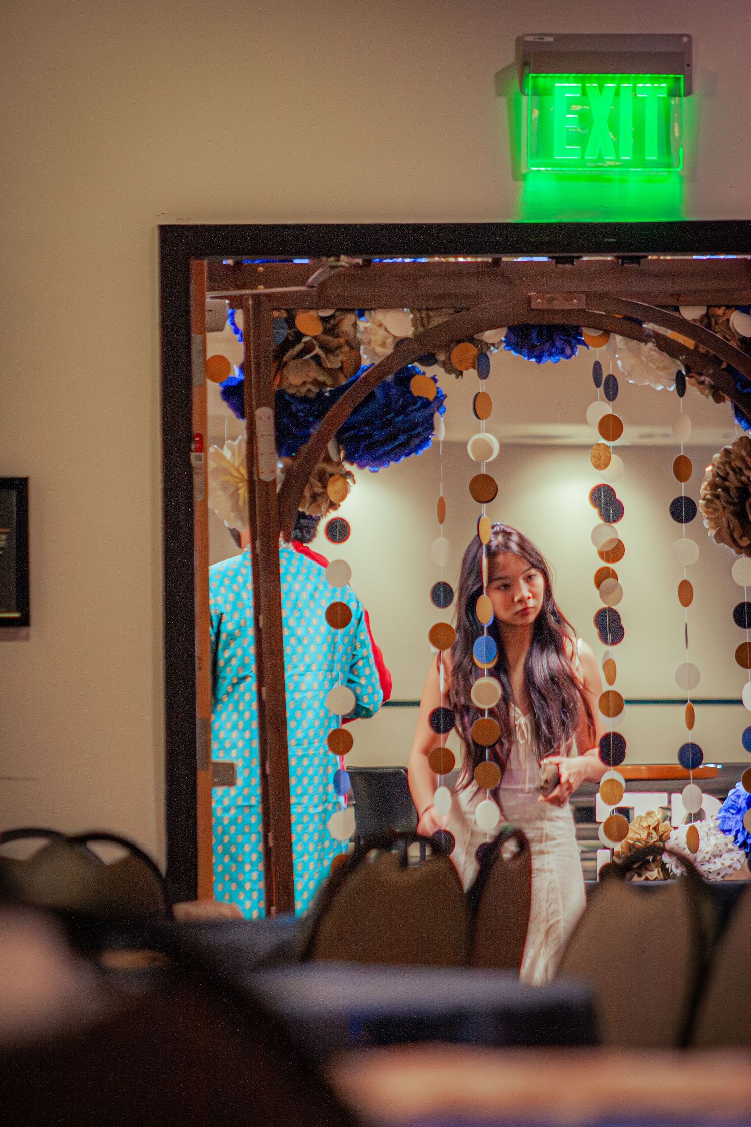 A young woman with long dark hair stands in a decorated doorway with circle garland decor.