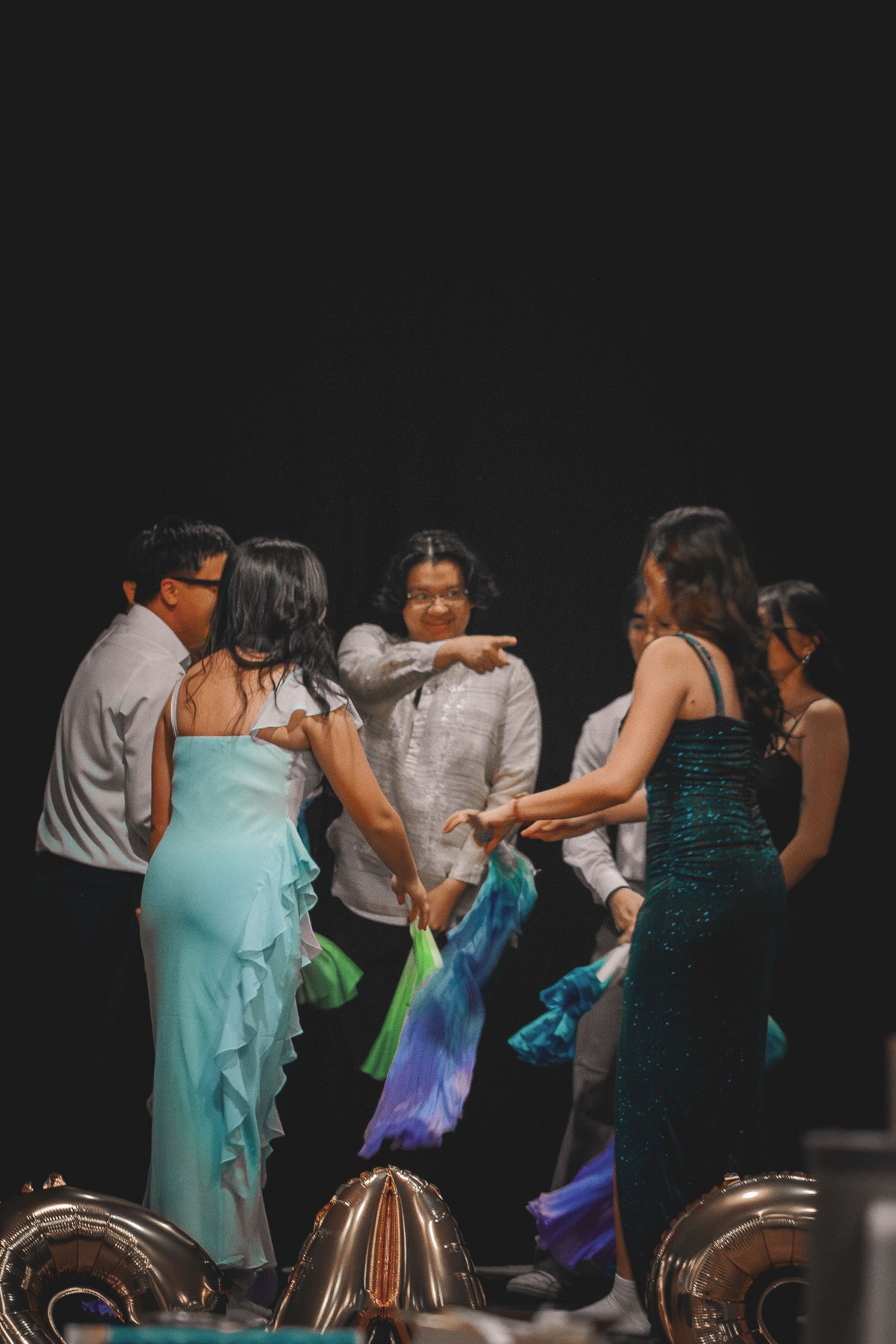 Group of young Asian performers in formal attire gathered together on stage after fan dance performance.