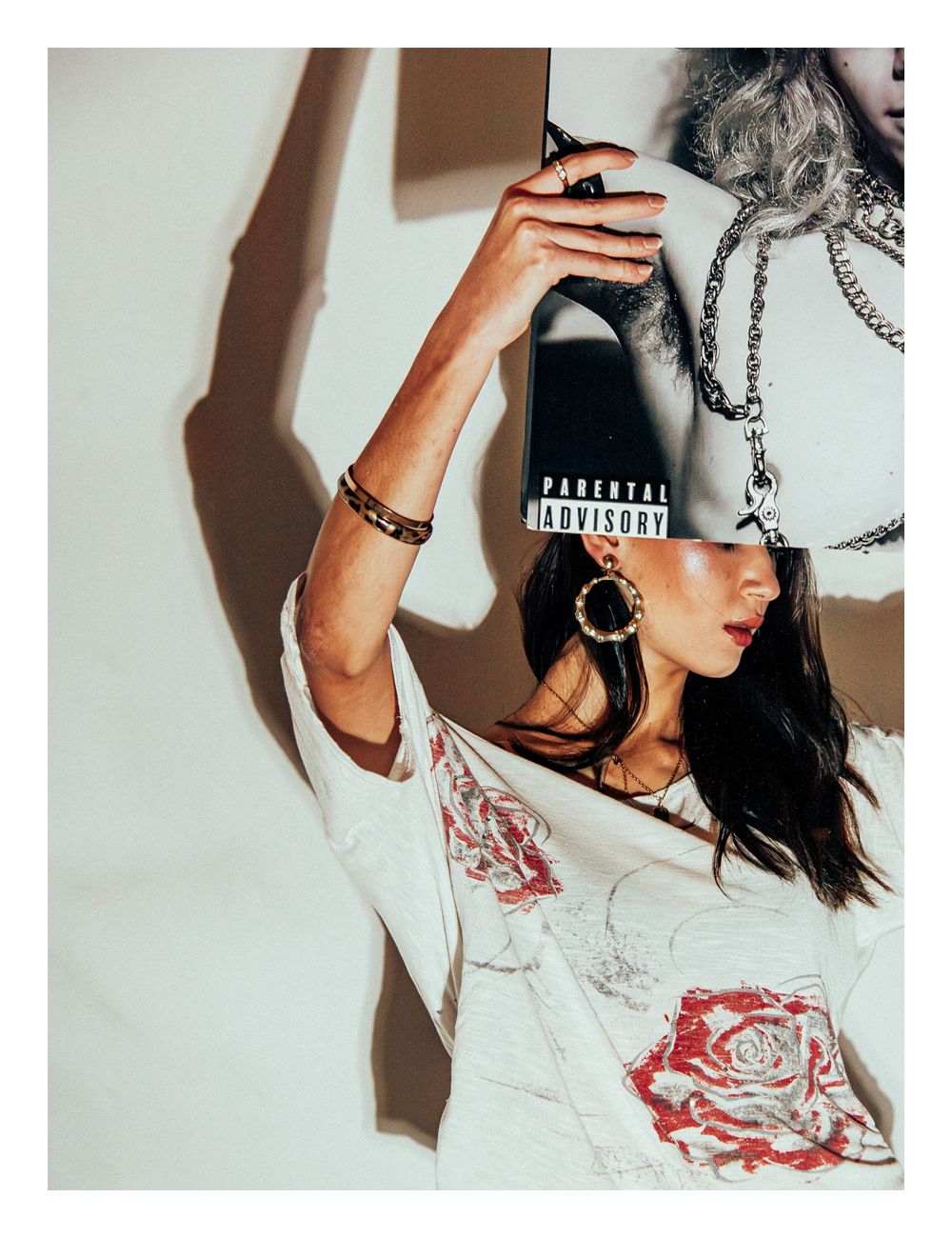 Woman in floral white top adjusts black Parental Advisory cap in editorial shot.