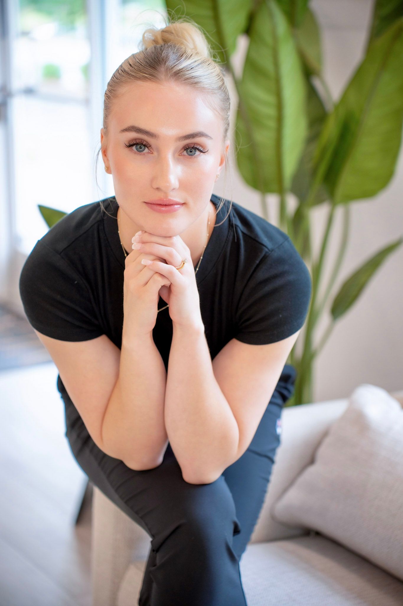 Portrait in black top against interior background with green plant.