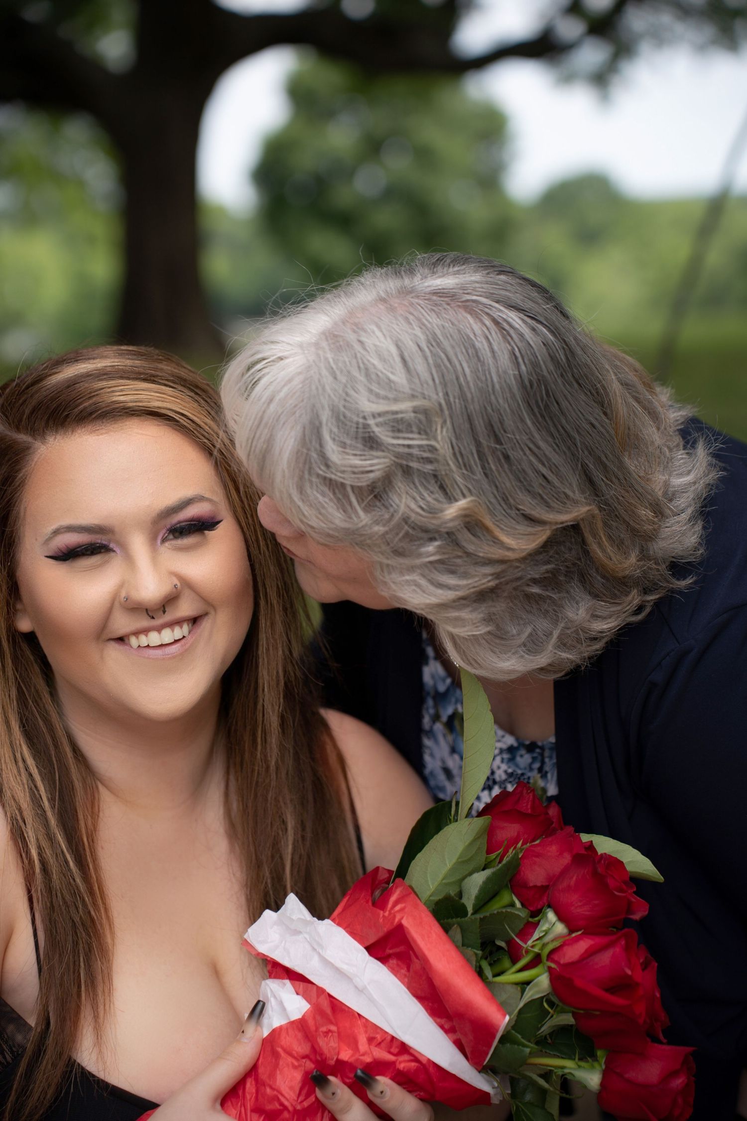 A heartwarming moment is shared between two people with red roses on a sunny day outdoors.